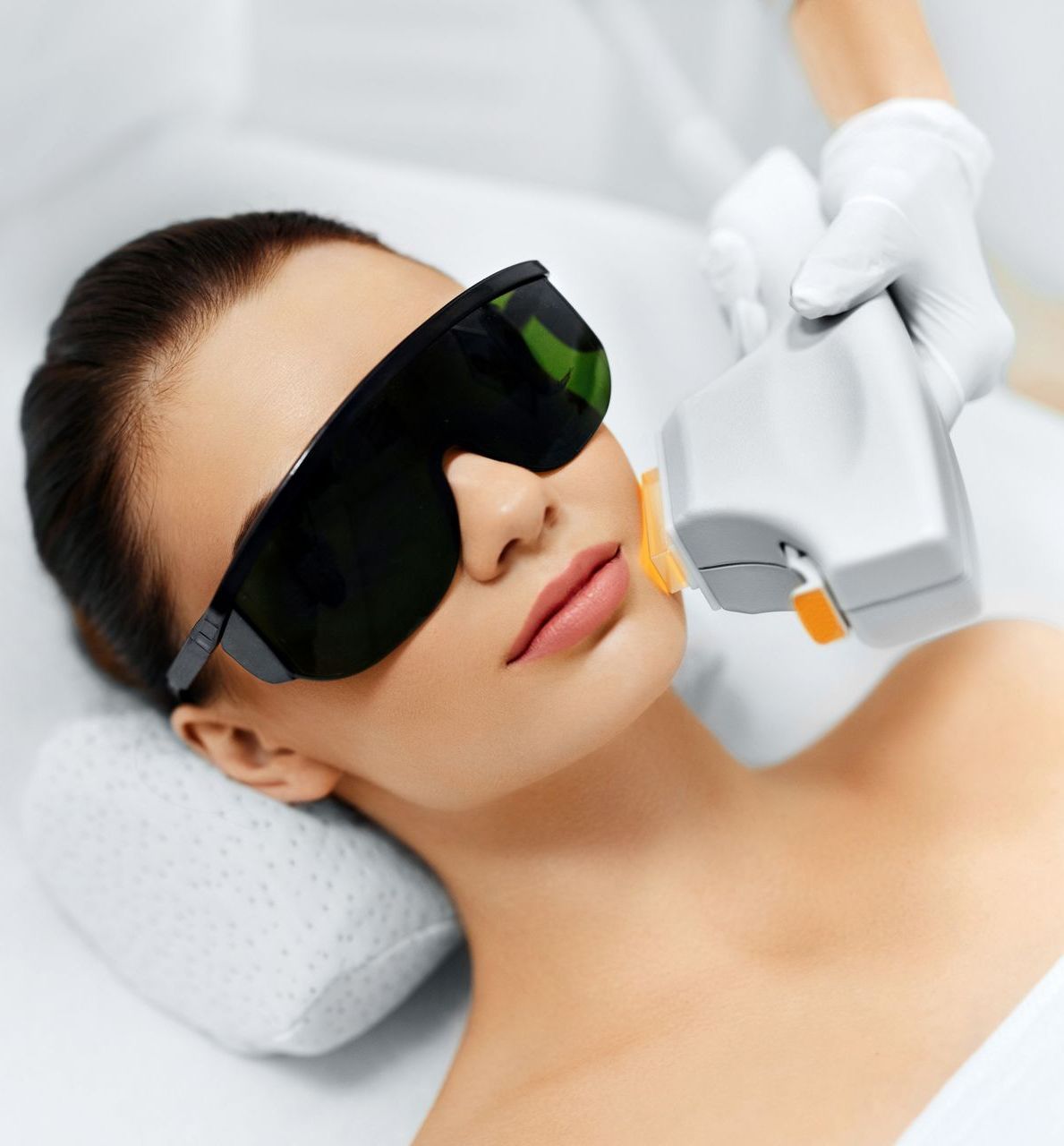 A woman wearing sunglasses is getting a laser treatment on her face
