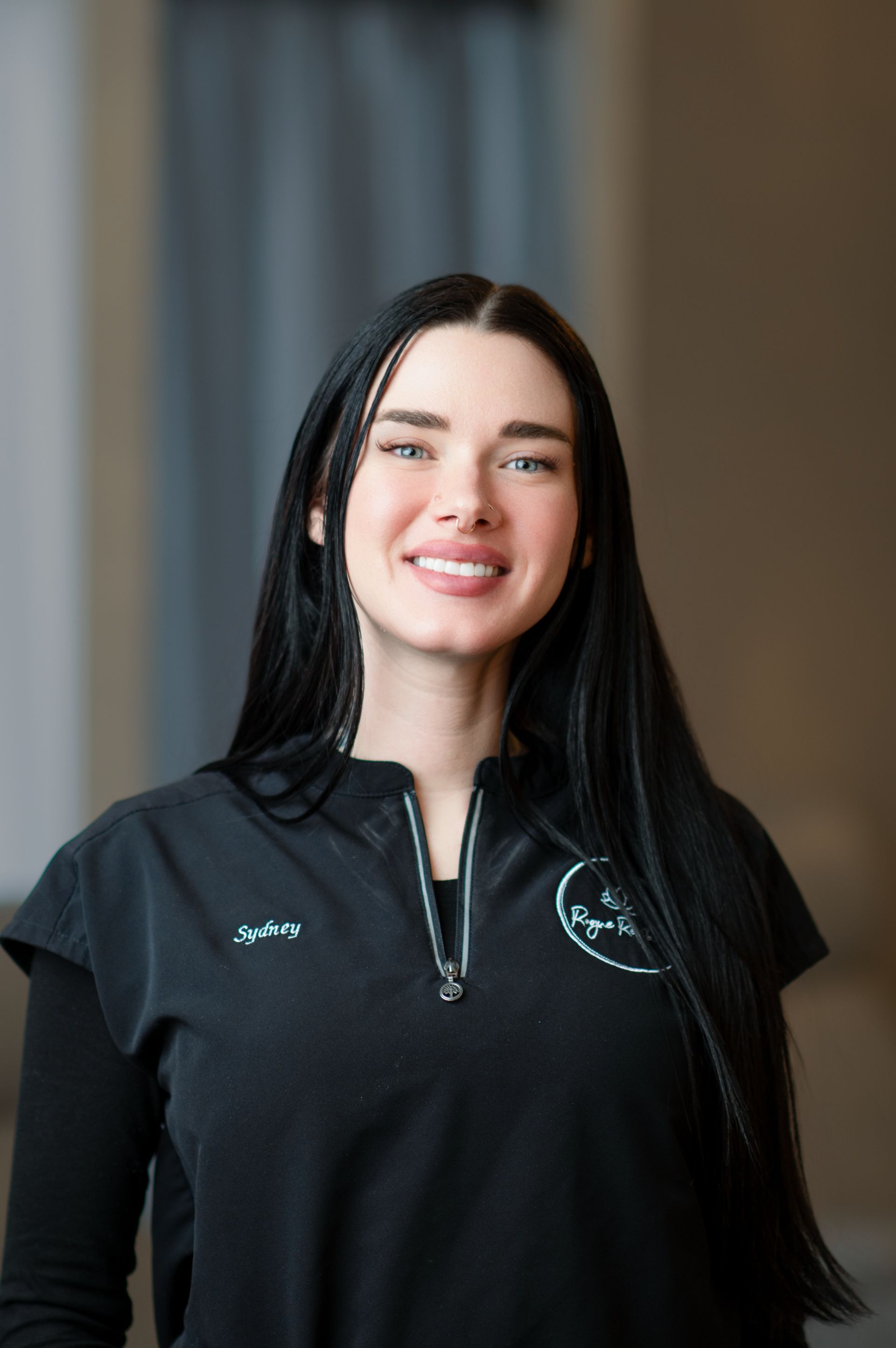 A woman with long black hair is wearing a black shirt and smiling.