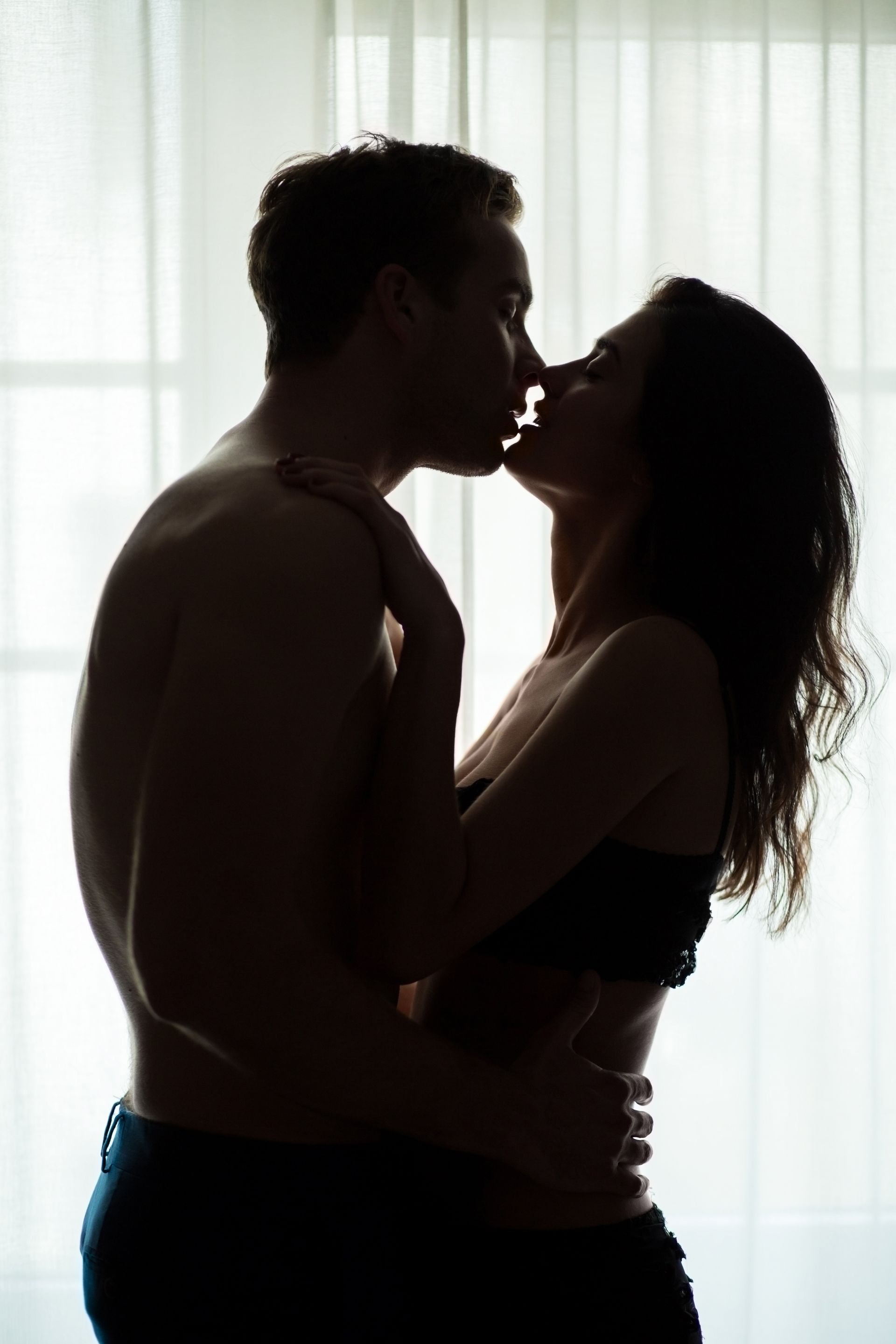 A man and a woman are kissing in front of a window.