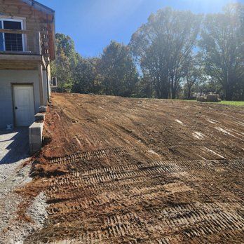 Dirt lot cleared next to a building with trees in the background on a sunny day.