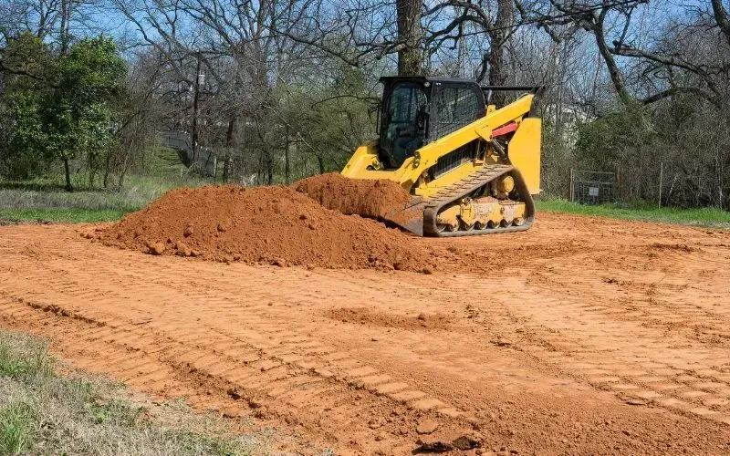 Yellow track loader pushing a pile of red dirt on a construction site.