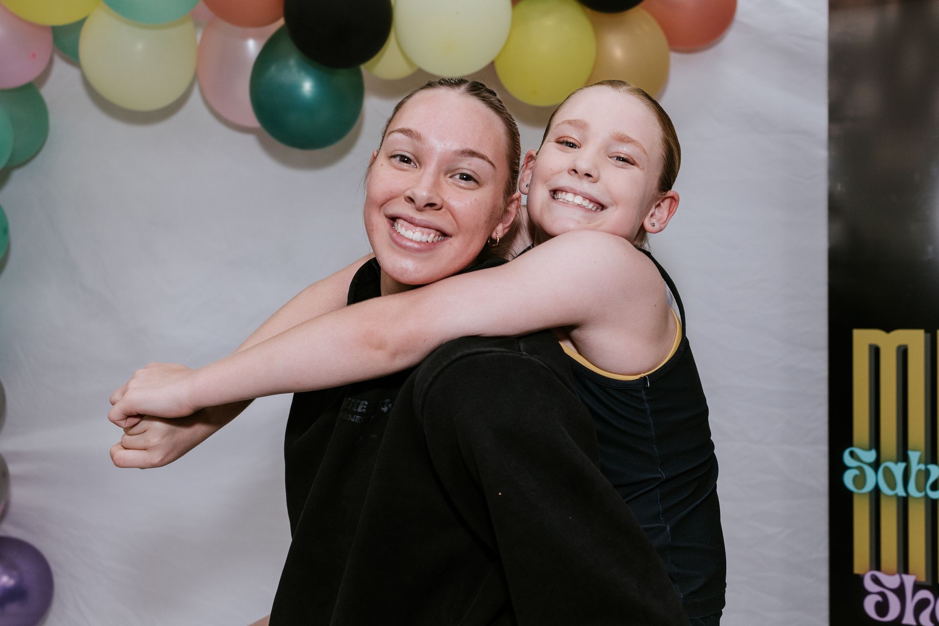 Two dancers in camouflage overalls on a stage; one sticks out their tongue.