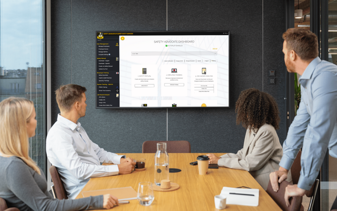 A group of people are sitting at a conference table in front of a flat screen tv.