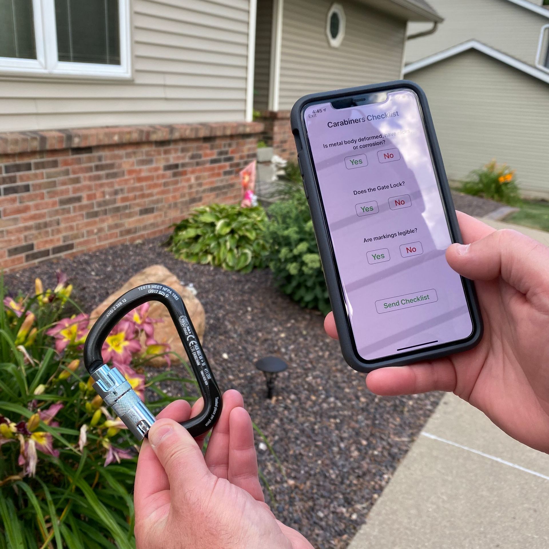 A person is holding a carabiner and a cell phone in front of a house.