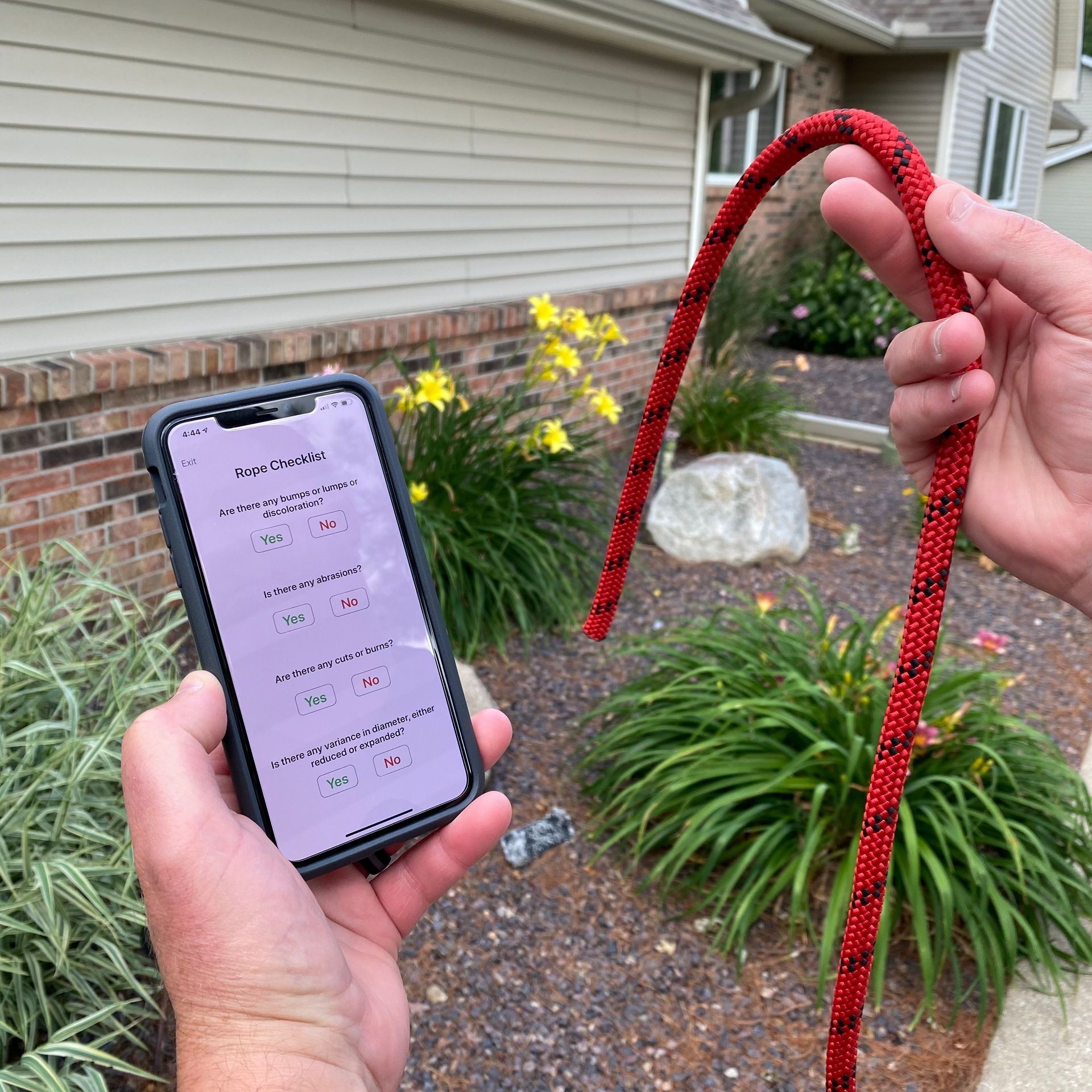 A person is holding a red rope and a cell phone in front of a house.