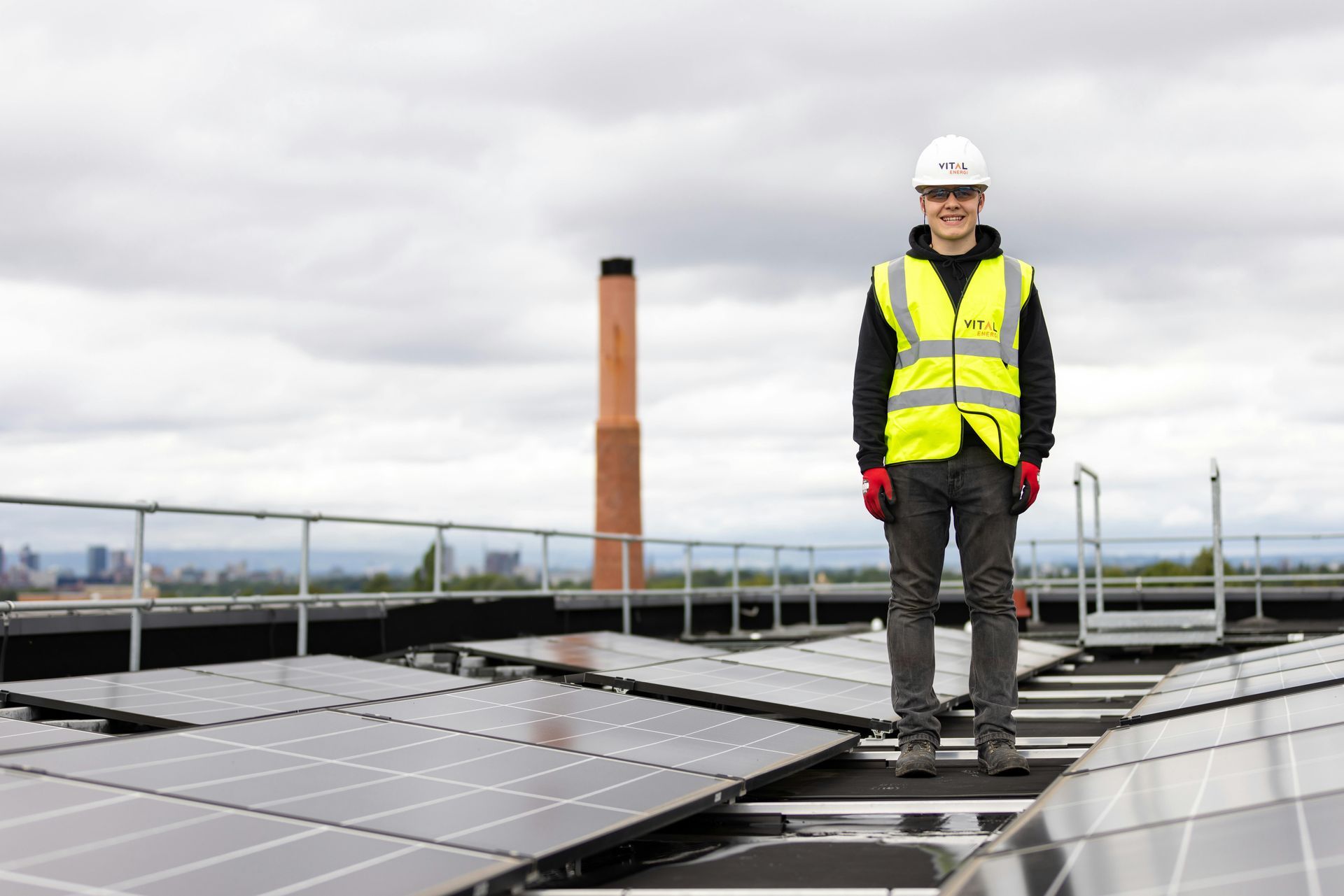 A man is standing on top of a roof with solar panels.