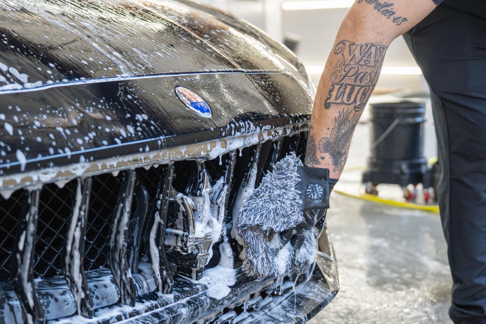 A person wearing gloves washes a black car grill with a soapy sponge.