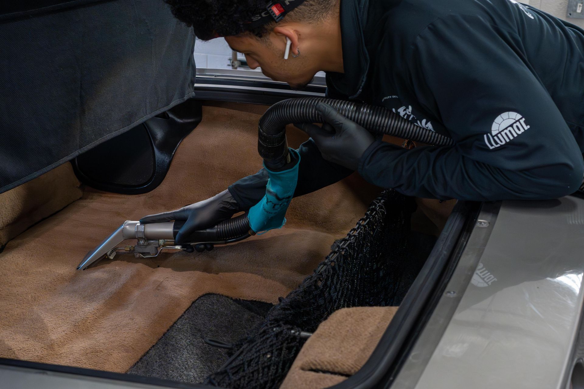 Person in black gloves cleaning a car interior with a vacuum. They are focused on cleaning the carpet.