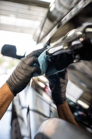 Person wearing black gloves cleaning a car door handle with a blue cloth.