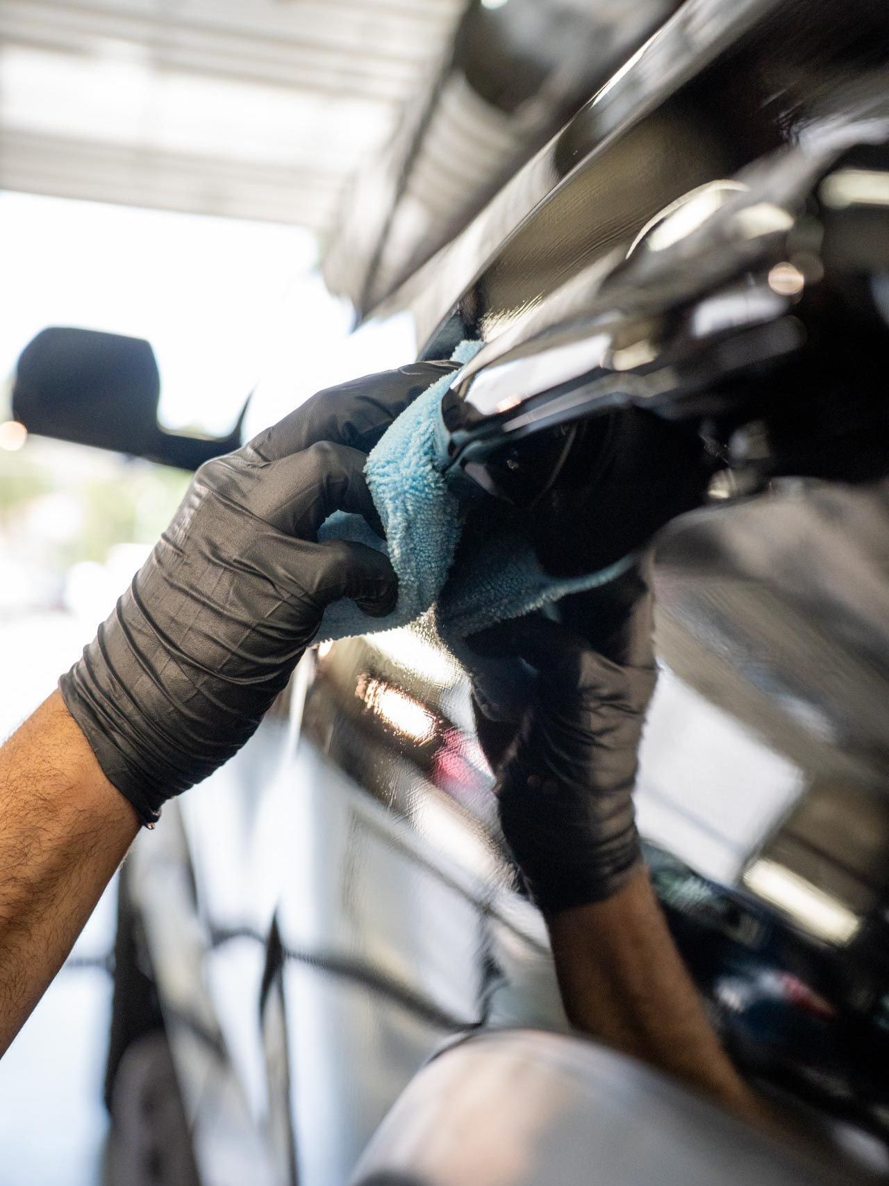 Person wearing black gloves wiping a black car door handle with a blue cloth.