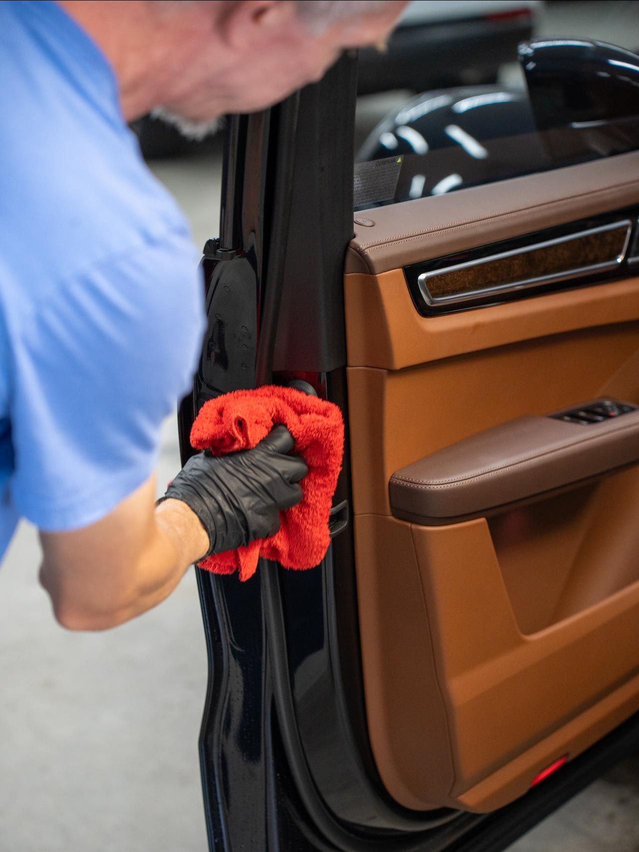 Person wearing black gloves wiping a black car door handle with a blue cloth.