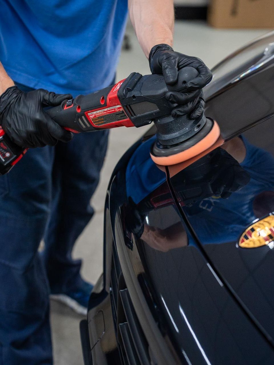 Person in black gloves polishing a black car with a red and black power buffer.