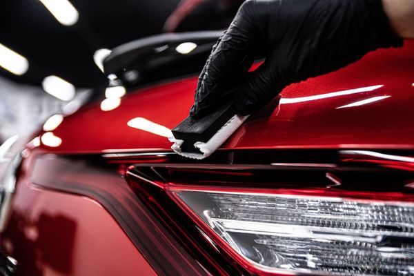 Gloved hand applying ceramic coating to a red car, near a headlight.