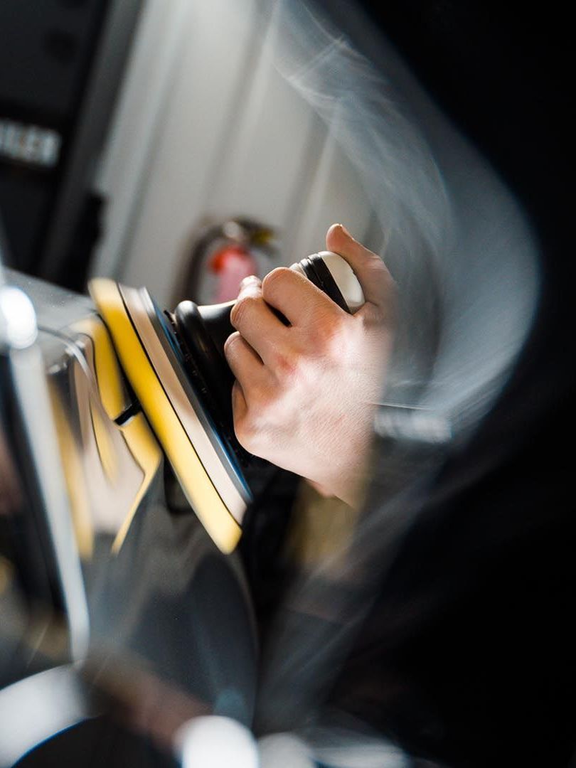 Person using a polishing tool on a dark vehicle, creating a blur effect as they work.