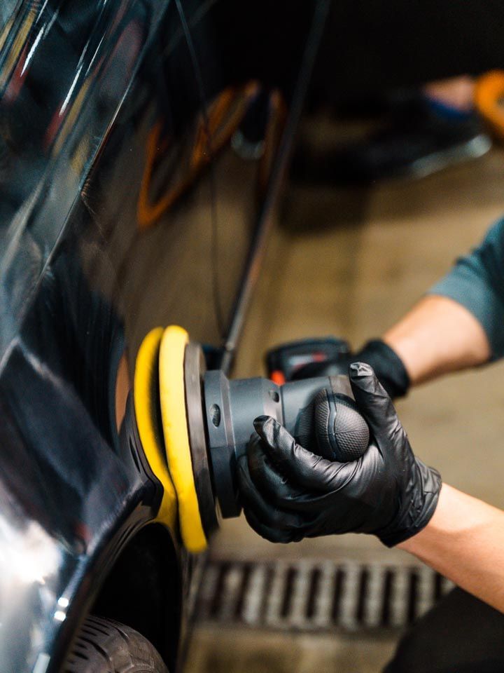 Person in black gloves polishing a black car with a yellow and black buffer.