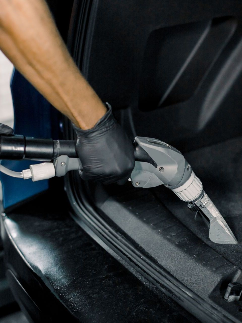 Person wearing black gloves wiping a black car door handle with a blue cloth.