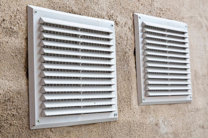 White plastic ventilation grille for internal air evacuation and bad smells with anti-insect net against a plaster wall