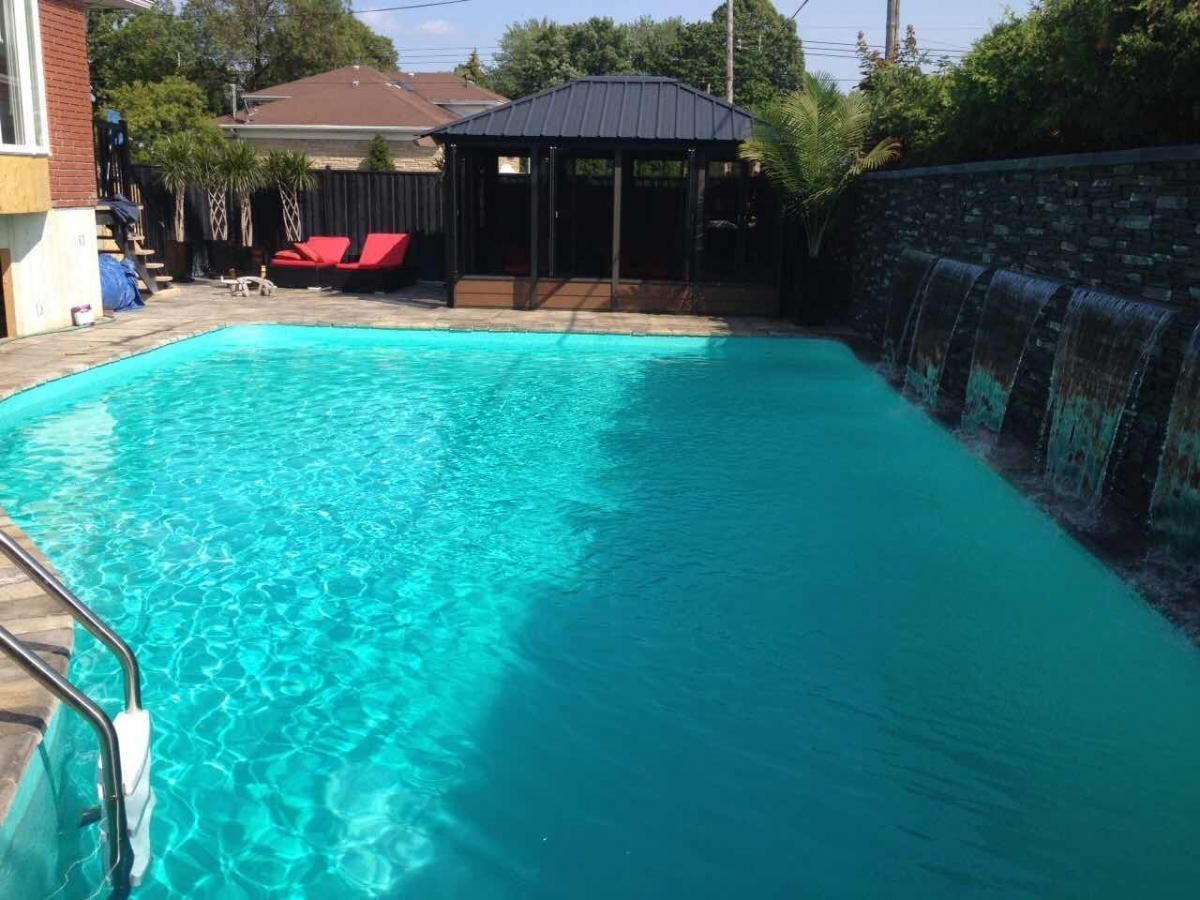 Une grande piscine avec un gazebo et une cascade dans l'arrière-cour.