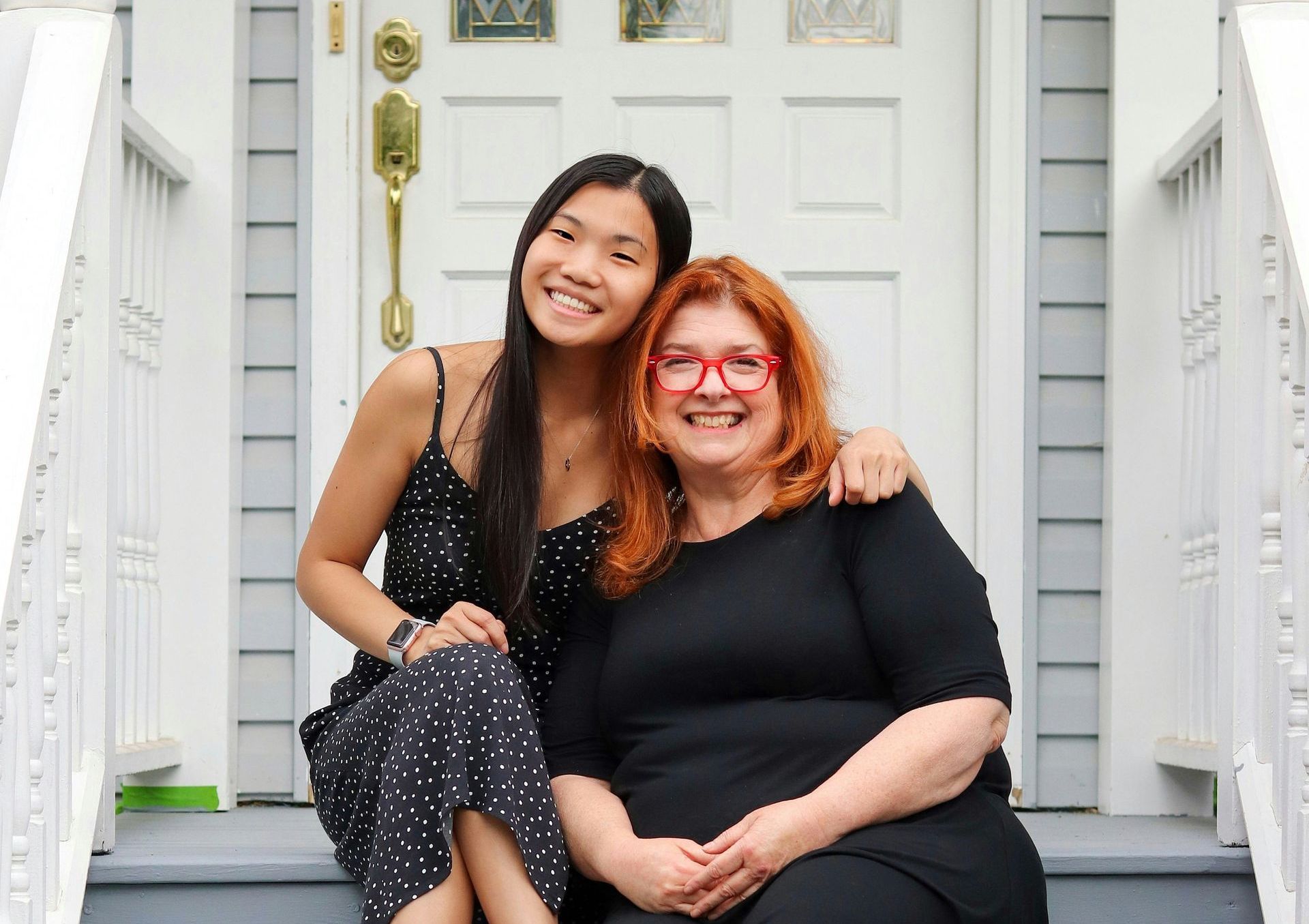 Two women are sitting on the porch of a house.