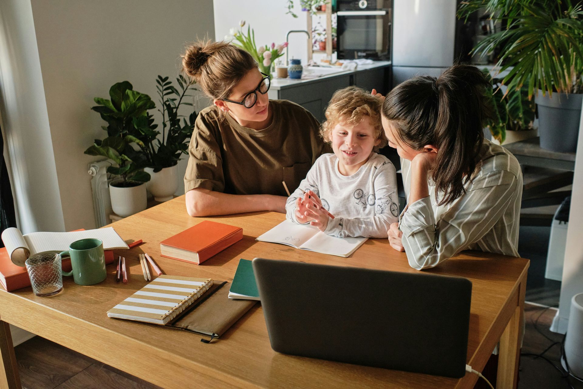 Three women are sitting at a table with a child and a laptop.