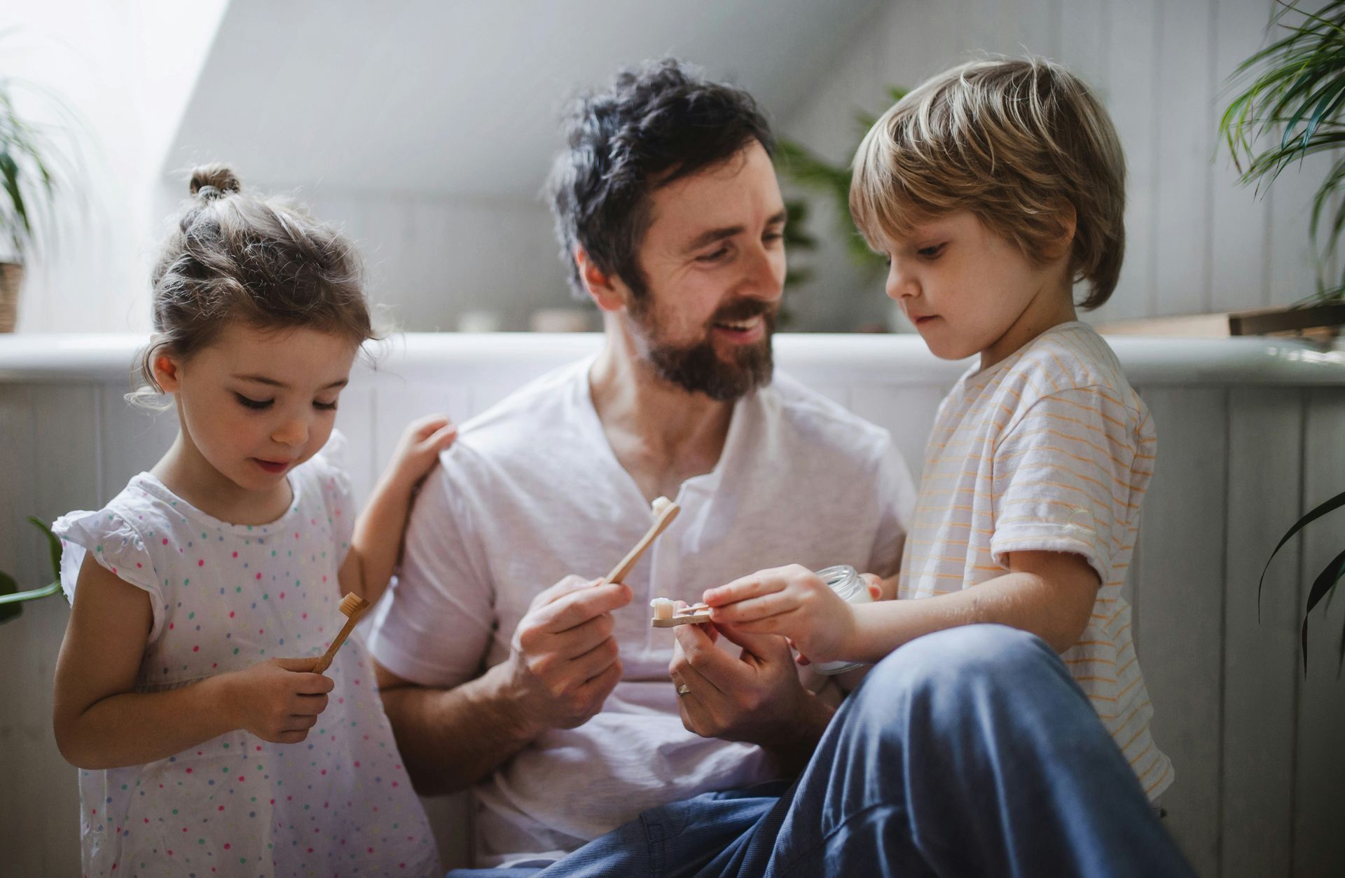 A man is brushing his teeth with two children.