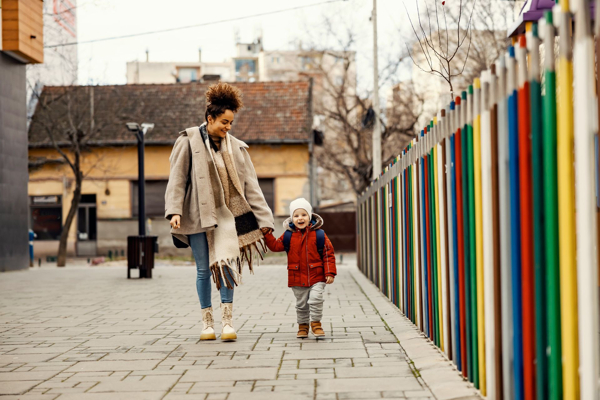 A woman and a child are walking down a sidewalk holding hands.