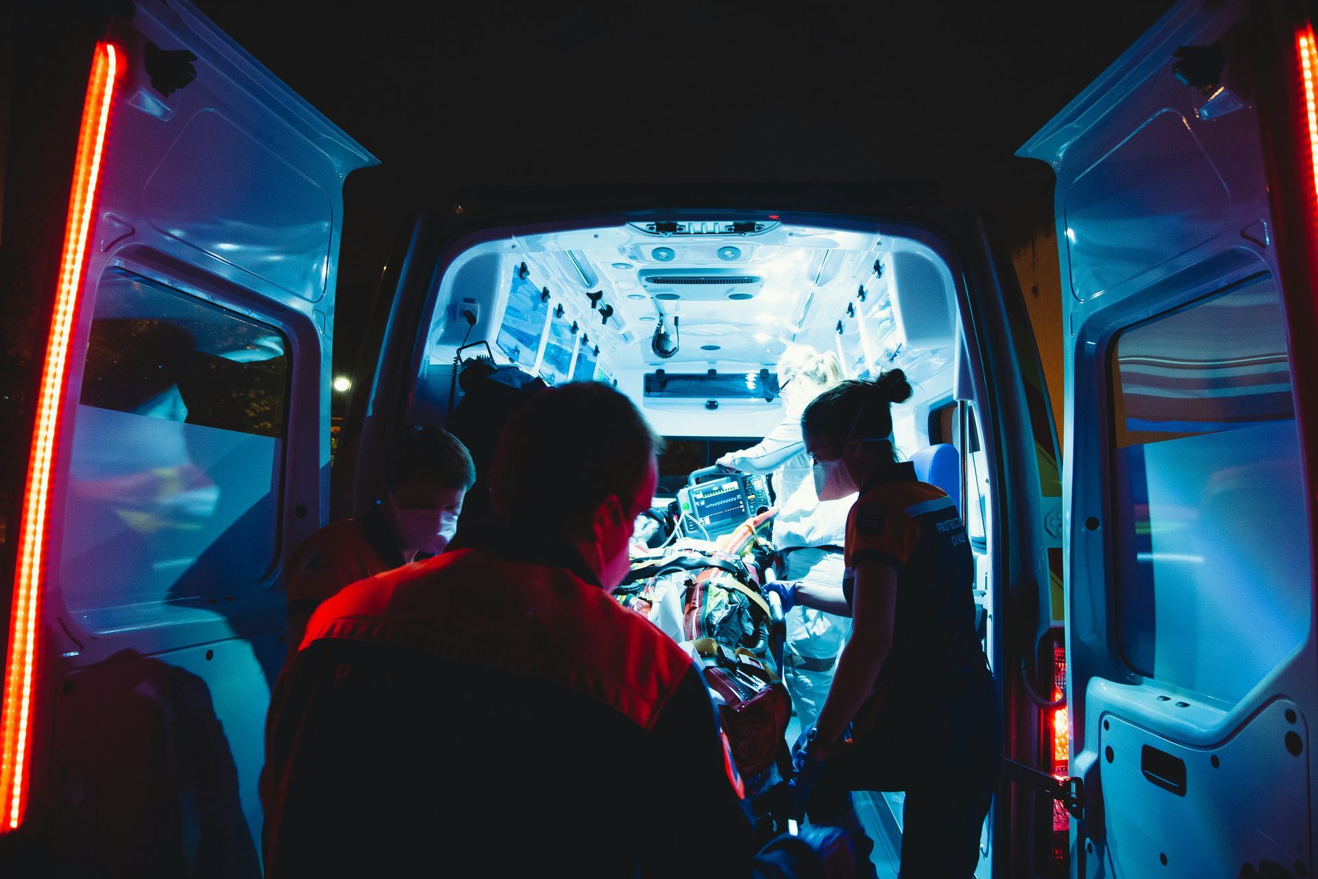 A couple of people are standing in the back of an ambulance at night.