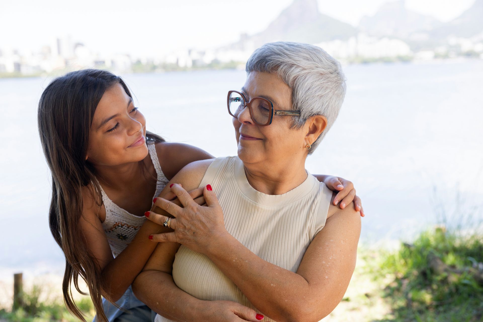 A little girl is hugging an older woman by the water.
