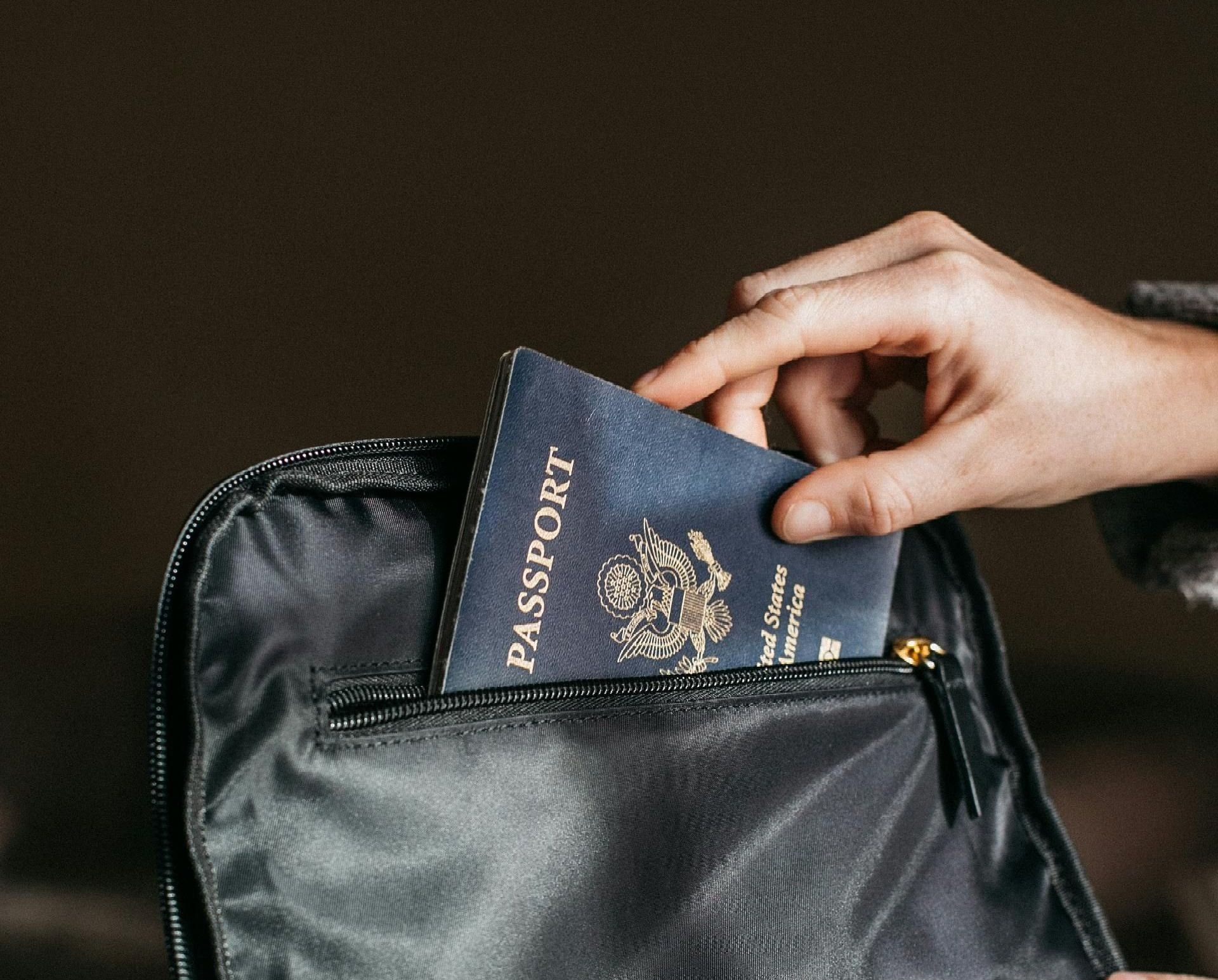 A person is putting a passport into a black bag.