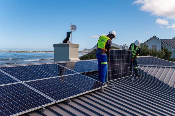 Two workers installing solar panels on a rooftop overlooking a coastal view.