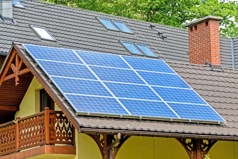 Solar panels installed on the roof of a house, with blue panels, a brown roof, and a chimney.