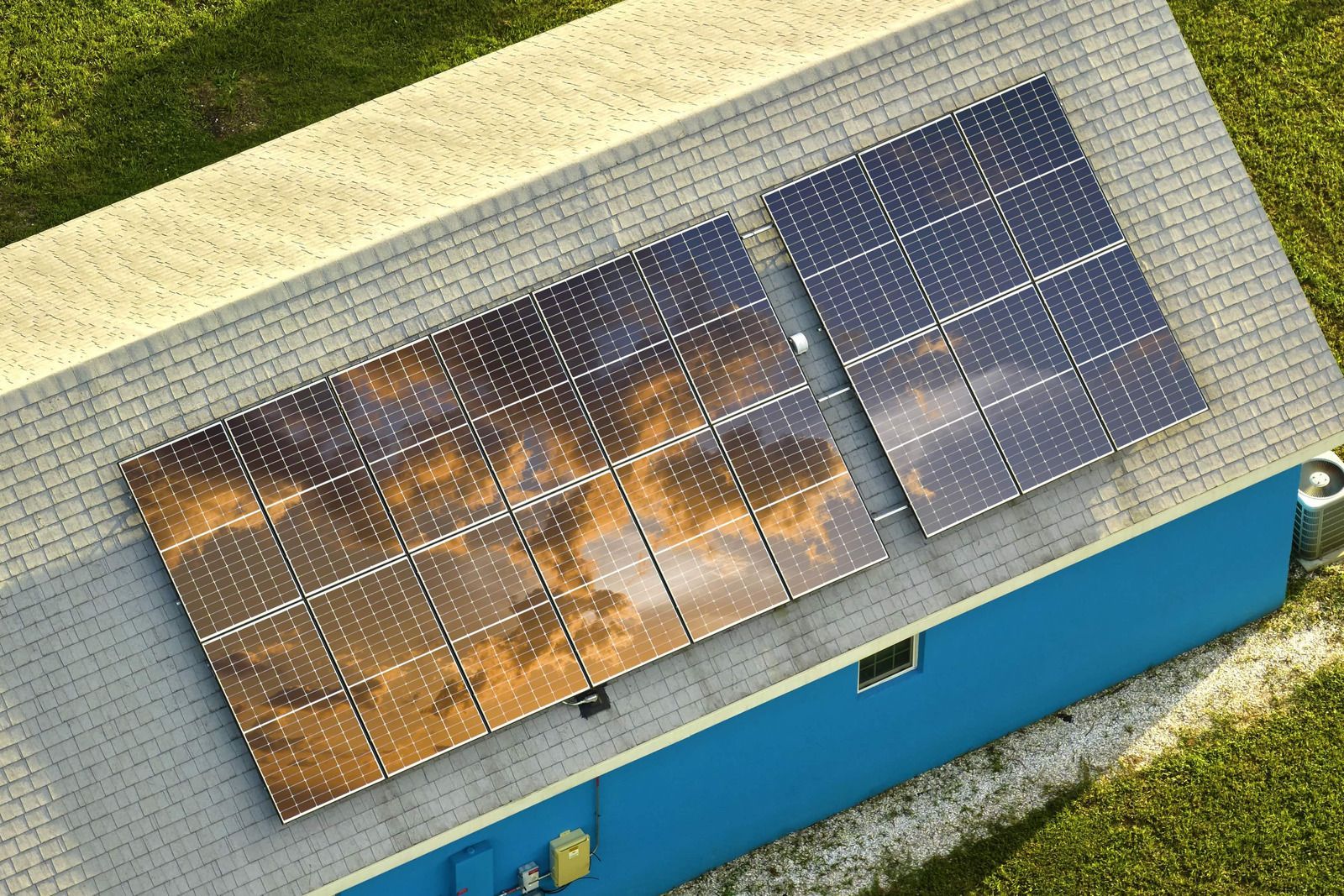 Solar panels on a roof, reflecting a cloudy sky, installed on a blue house.