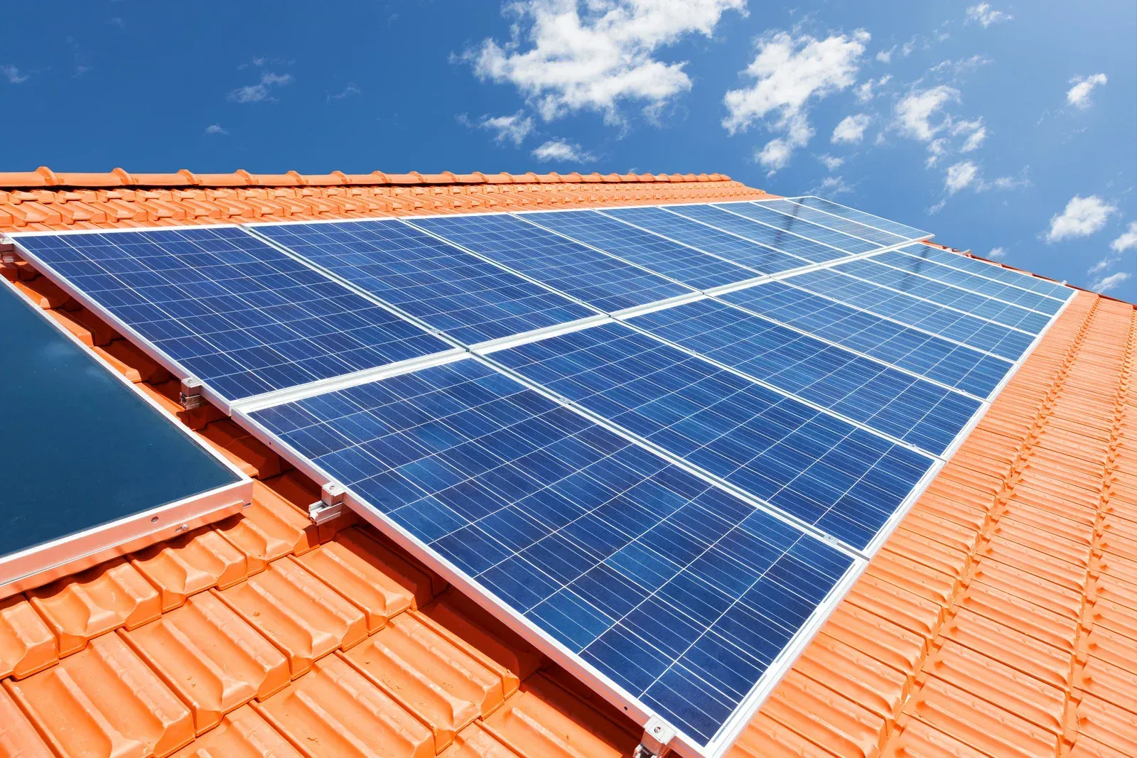 Solar panels installed on a red tile roof against a blue sky with white clouds.