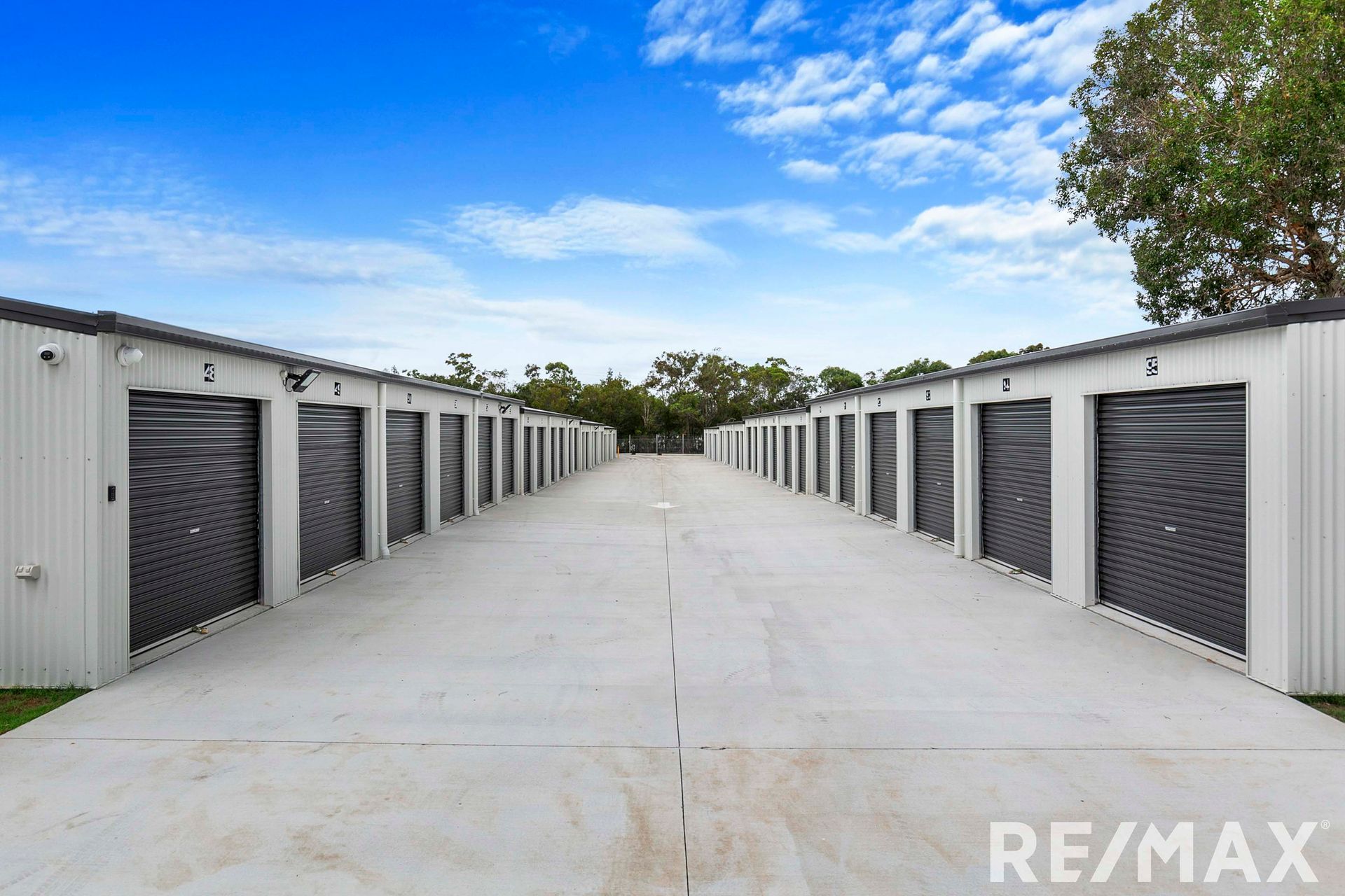 Row of storage units with gray doors and white siding under a blue sky.