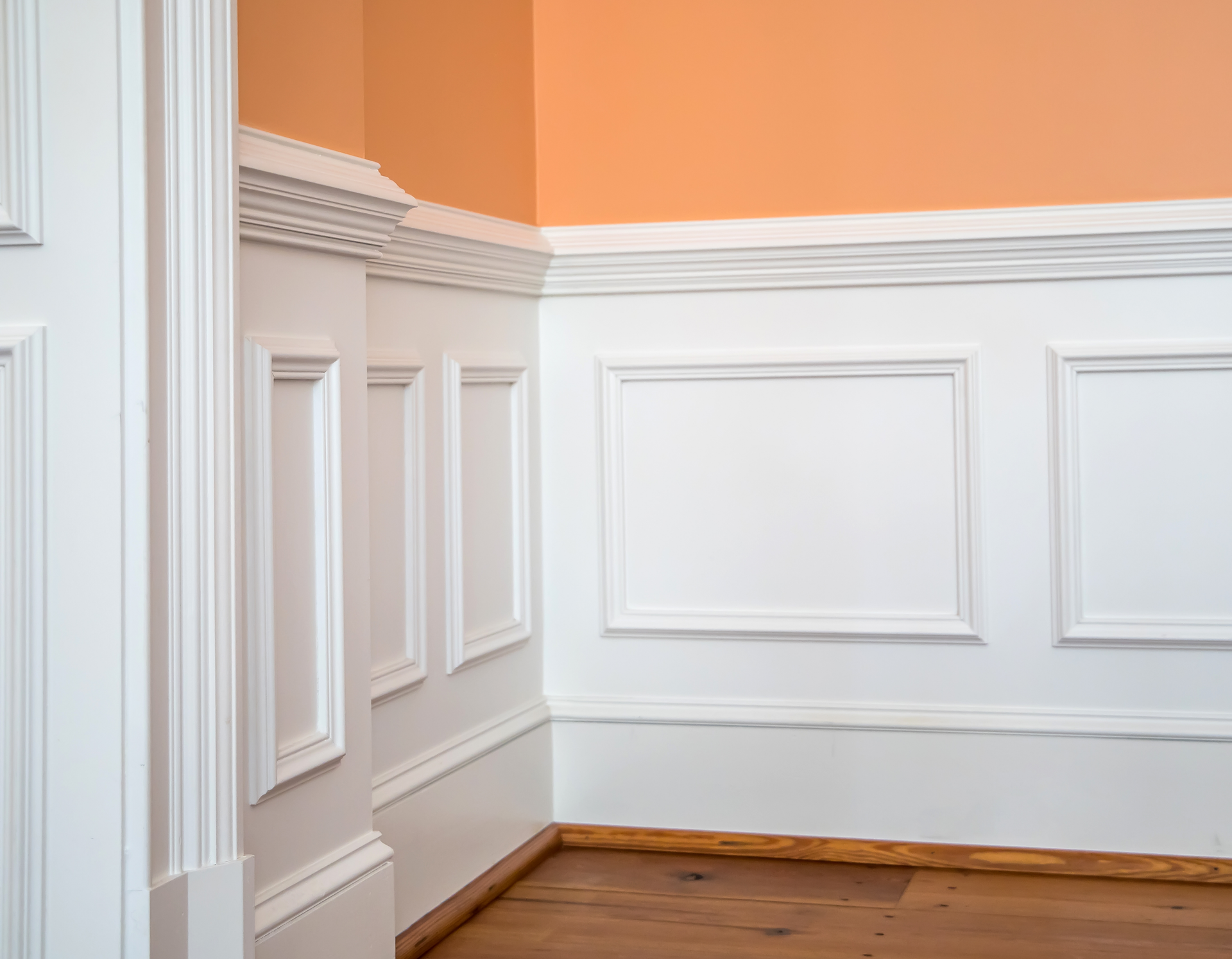 A corner of a room with white paneling and orange walls.