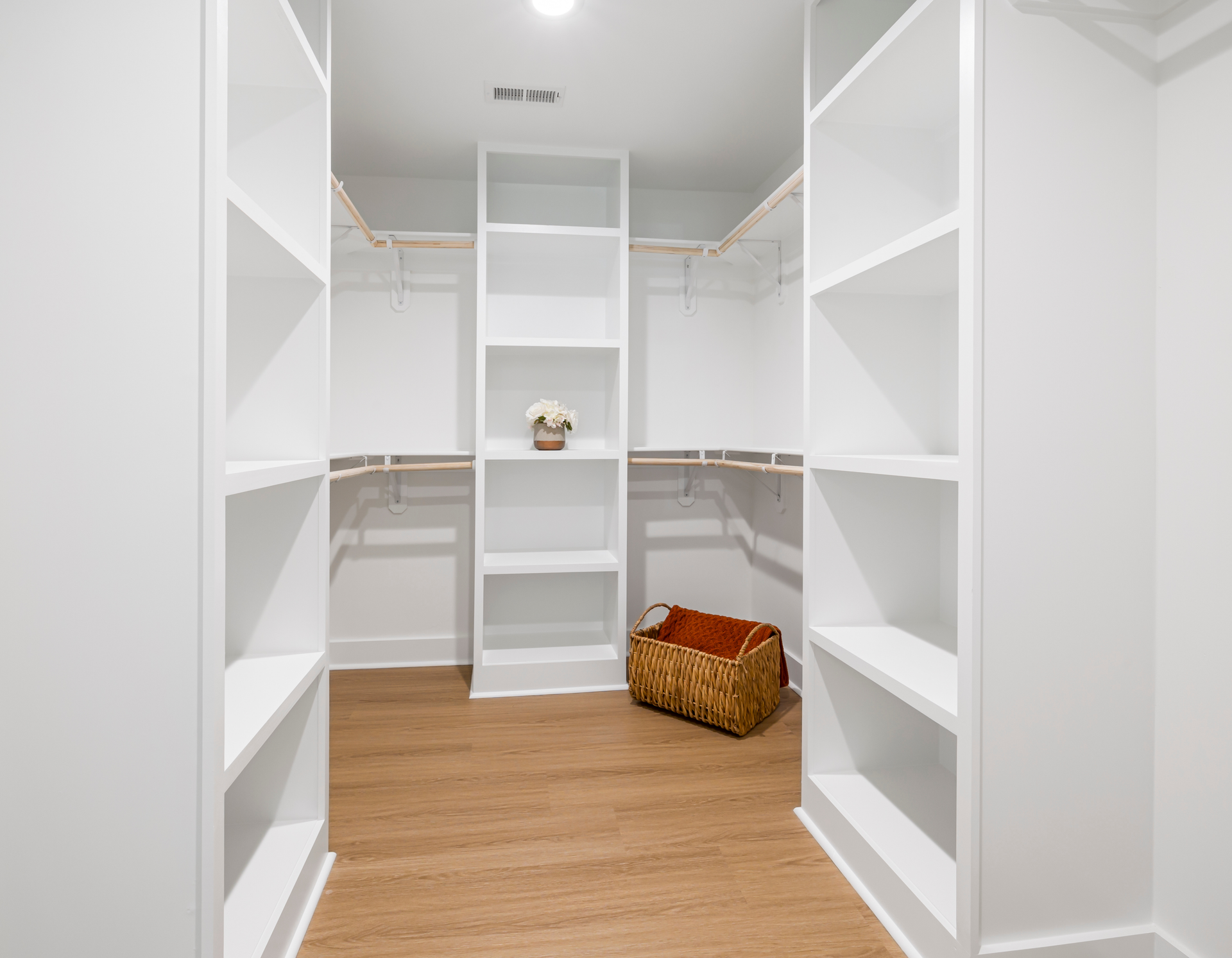 A walk in closet with lots of shelves and a basket on the floor.