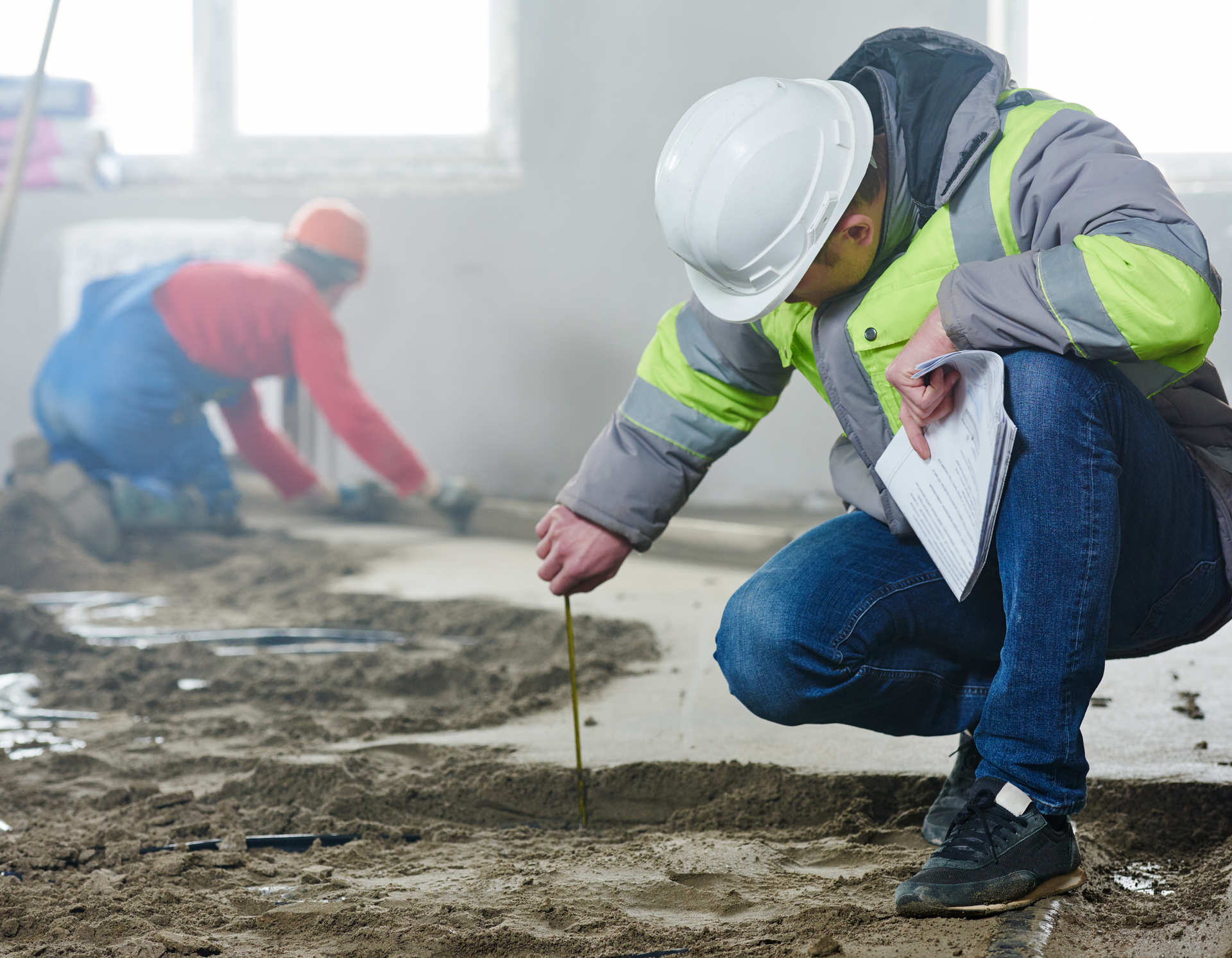A construction worker is measuring the floor with a tape measure.