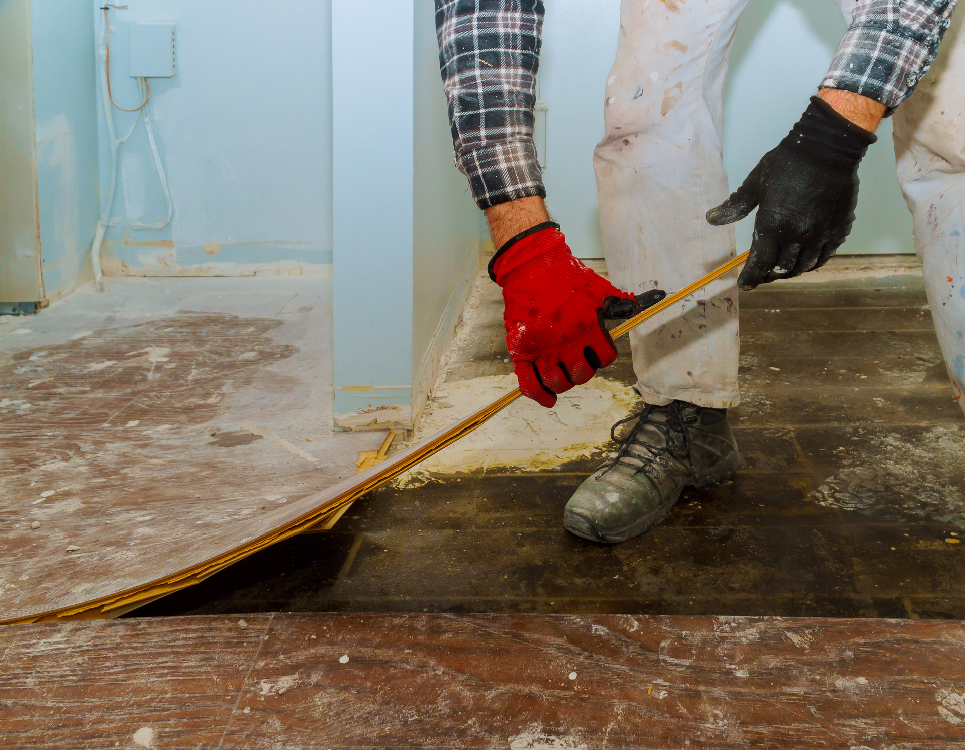 A man wearing red gloves is measuring a piece of wood with a tape measure.