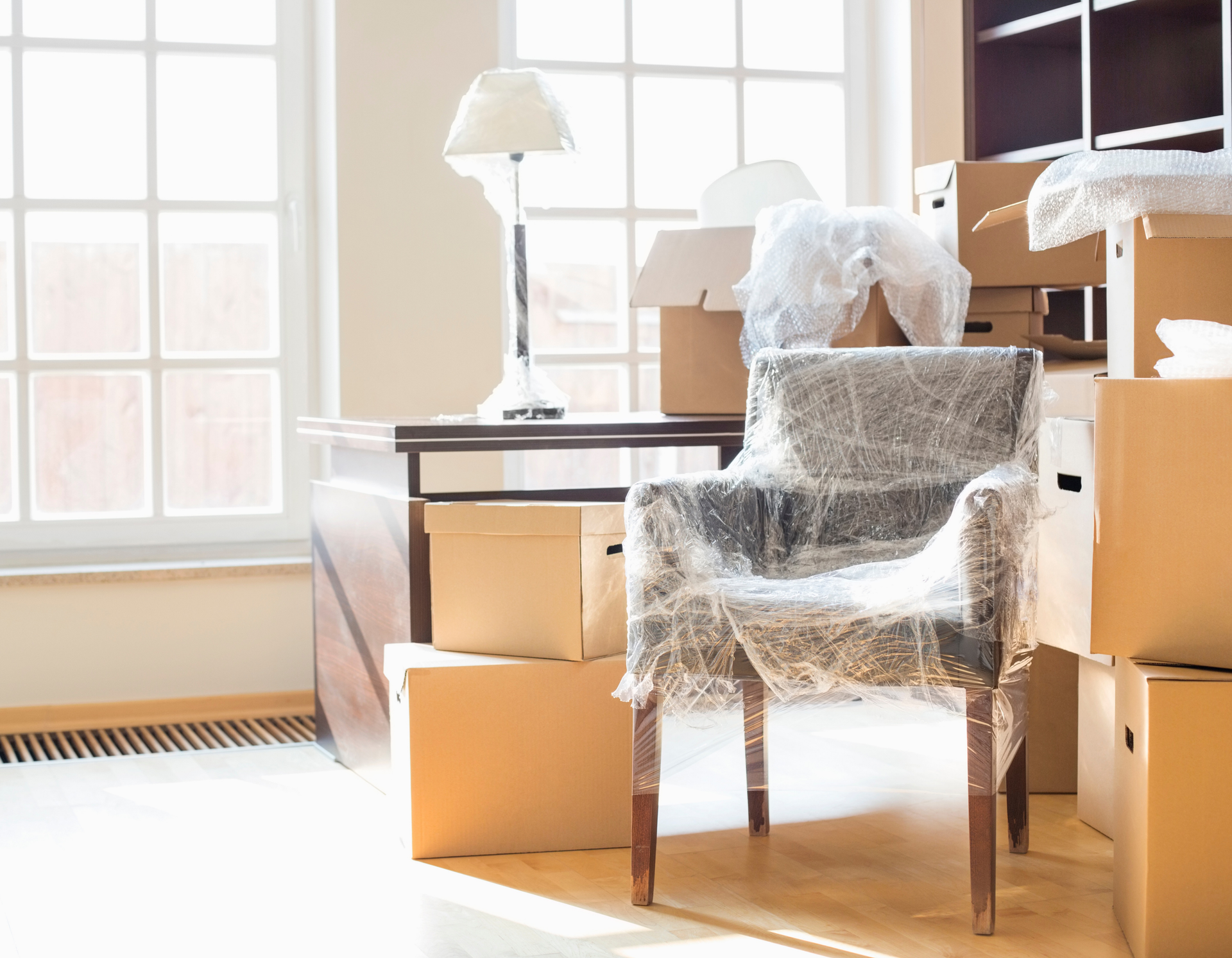 A chair wrapped in plastic is sitting in a room surrounded by cardboard boxes.