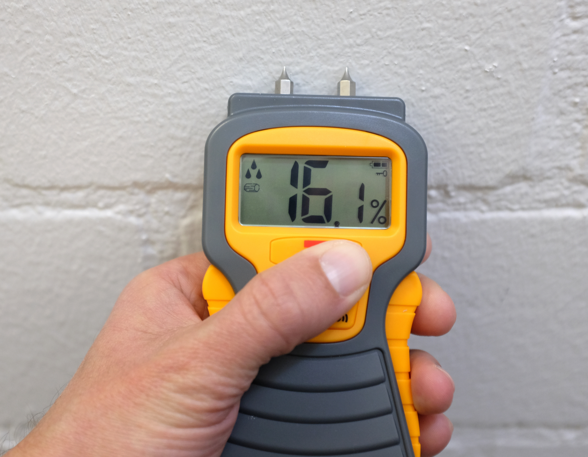 A hand is holding a digital humidity meter that reads 16.1%
