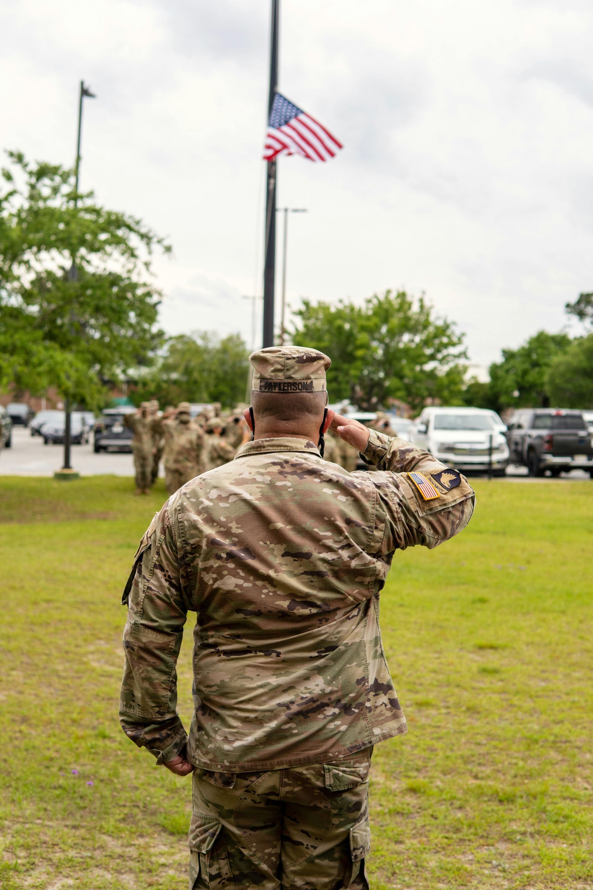 A soldier is saluting the american flag while standing in front of a flag pole.