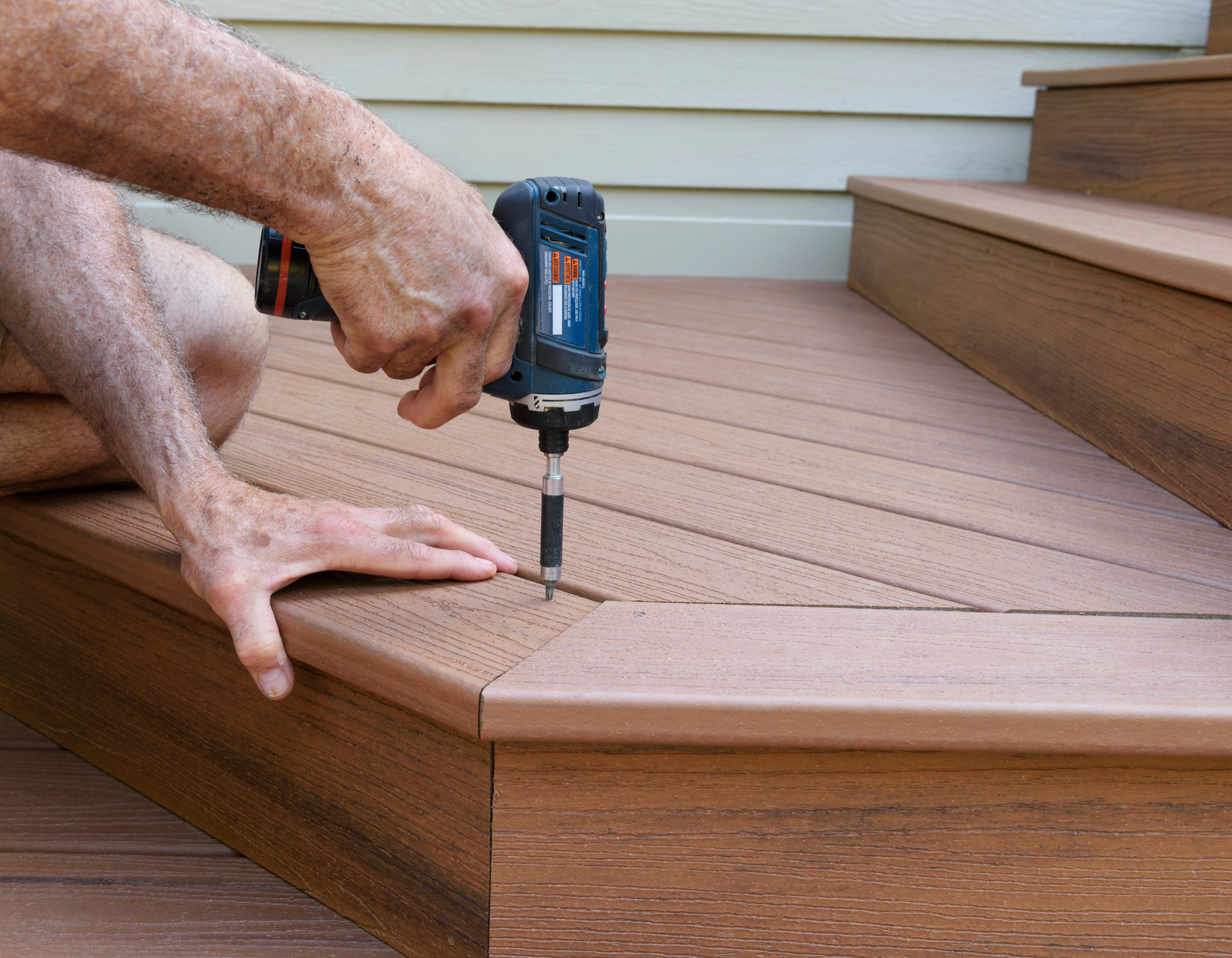 A man is using a drill on a wooden deck.