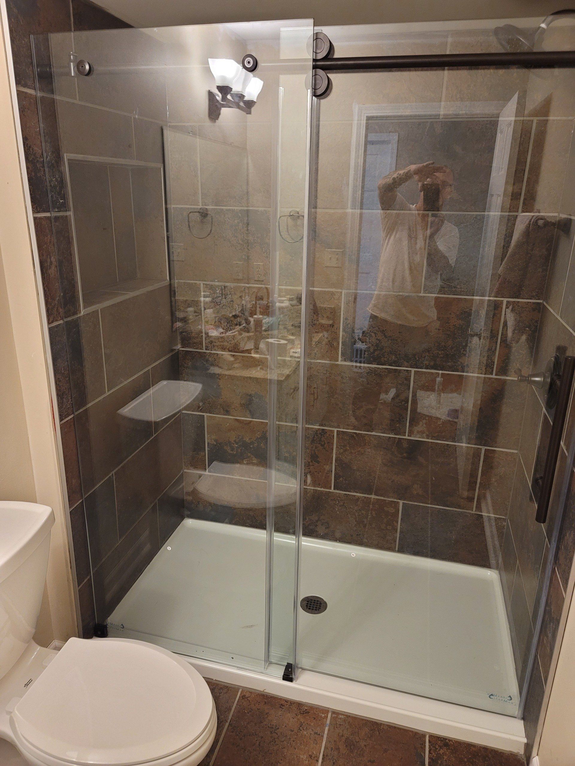 Shower with glass doors and brown tile. A toilet is in the foreground.