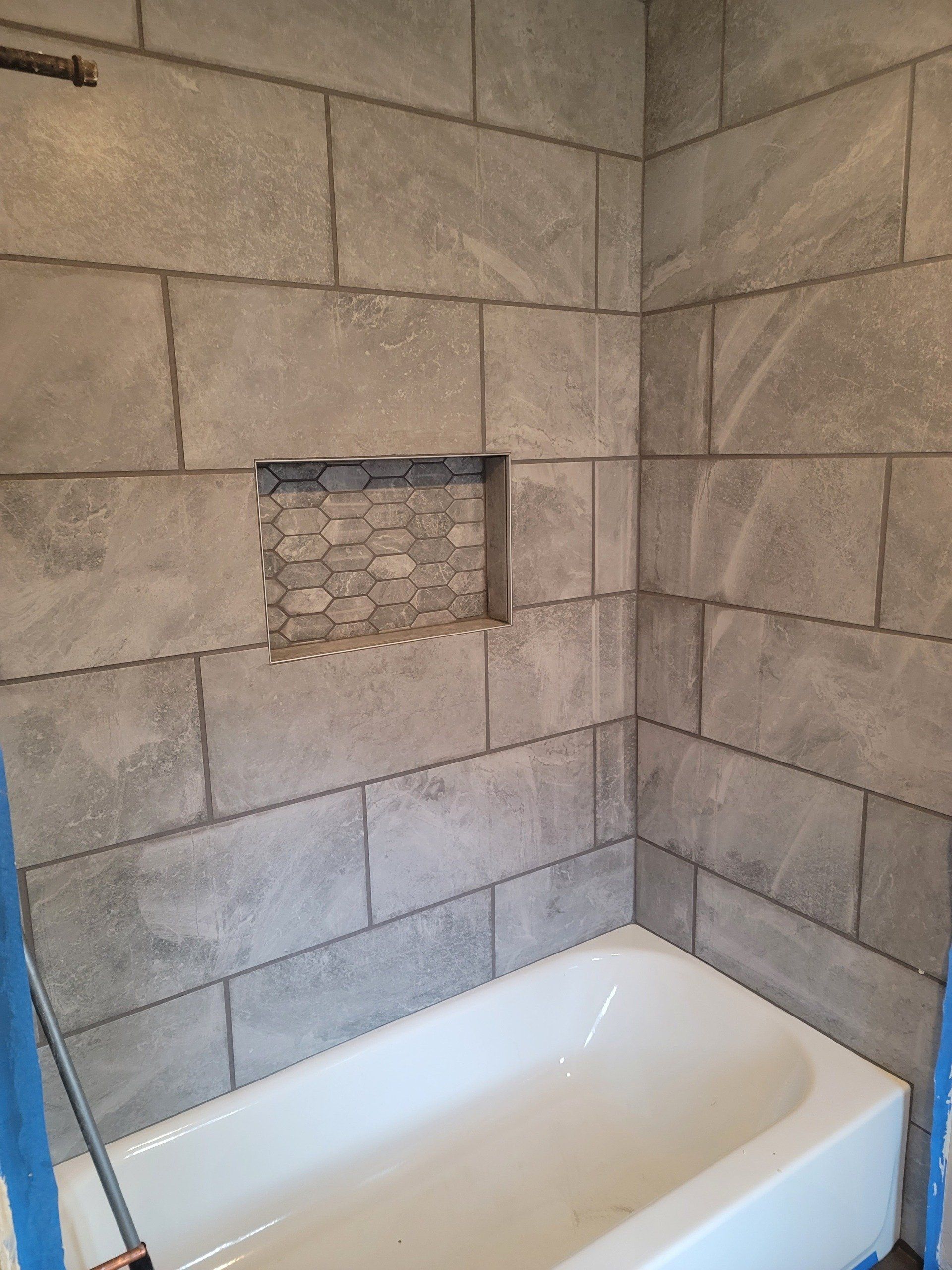 A bathtub is sitting in a bathroom next to a tiled wall.