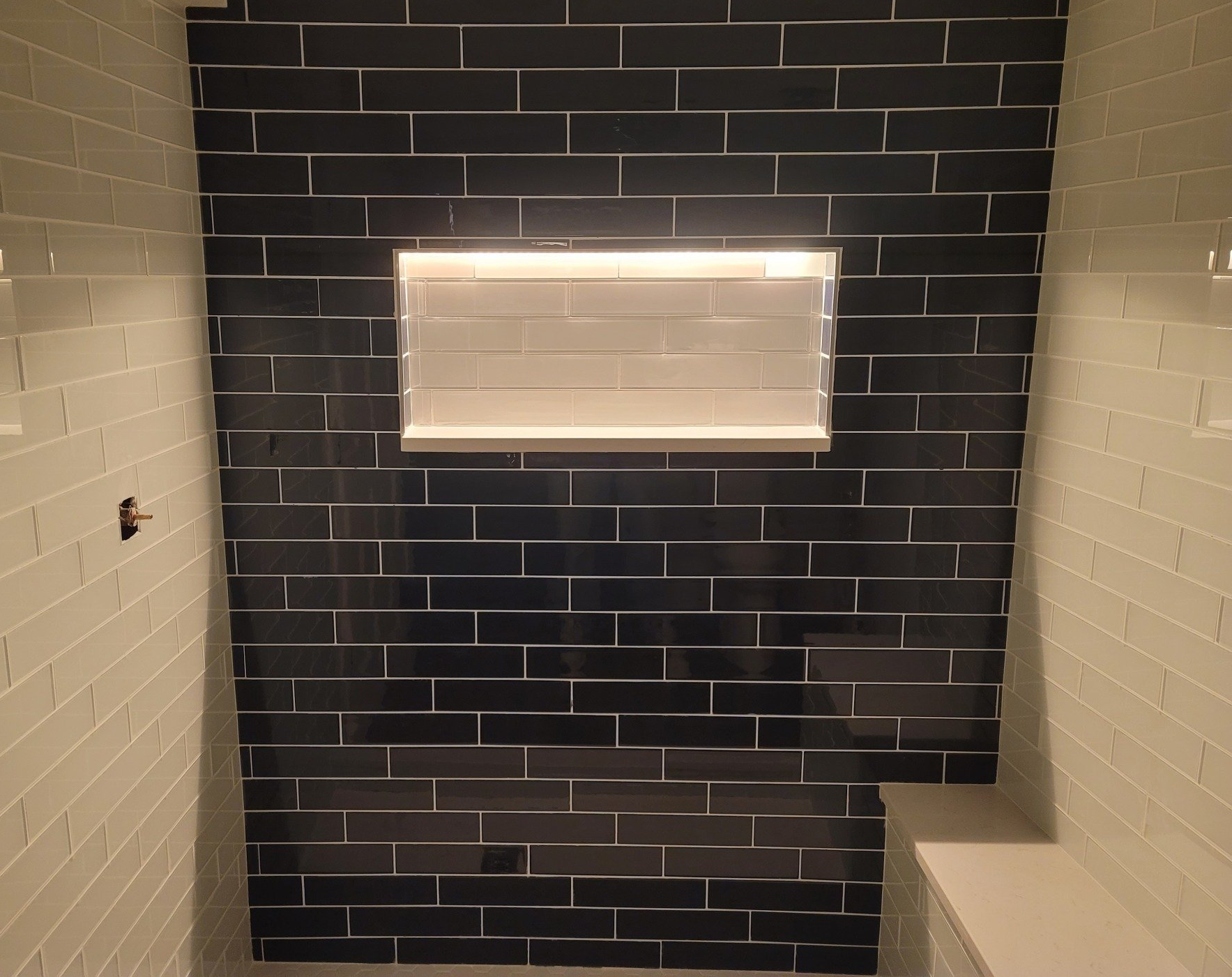 Black and white tiled shower with a niche lit from within.