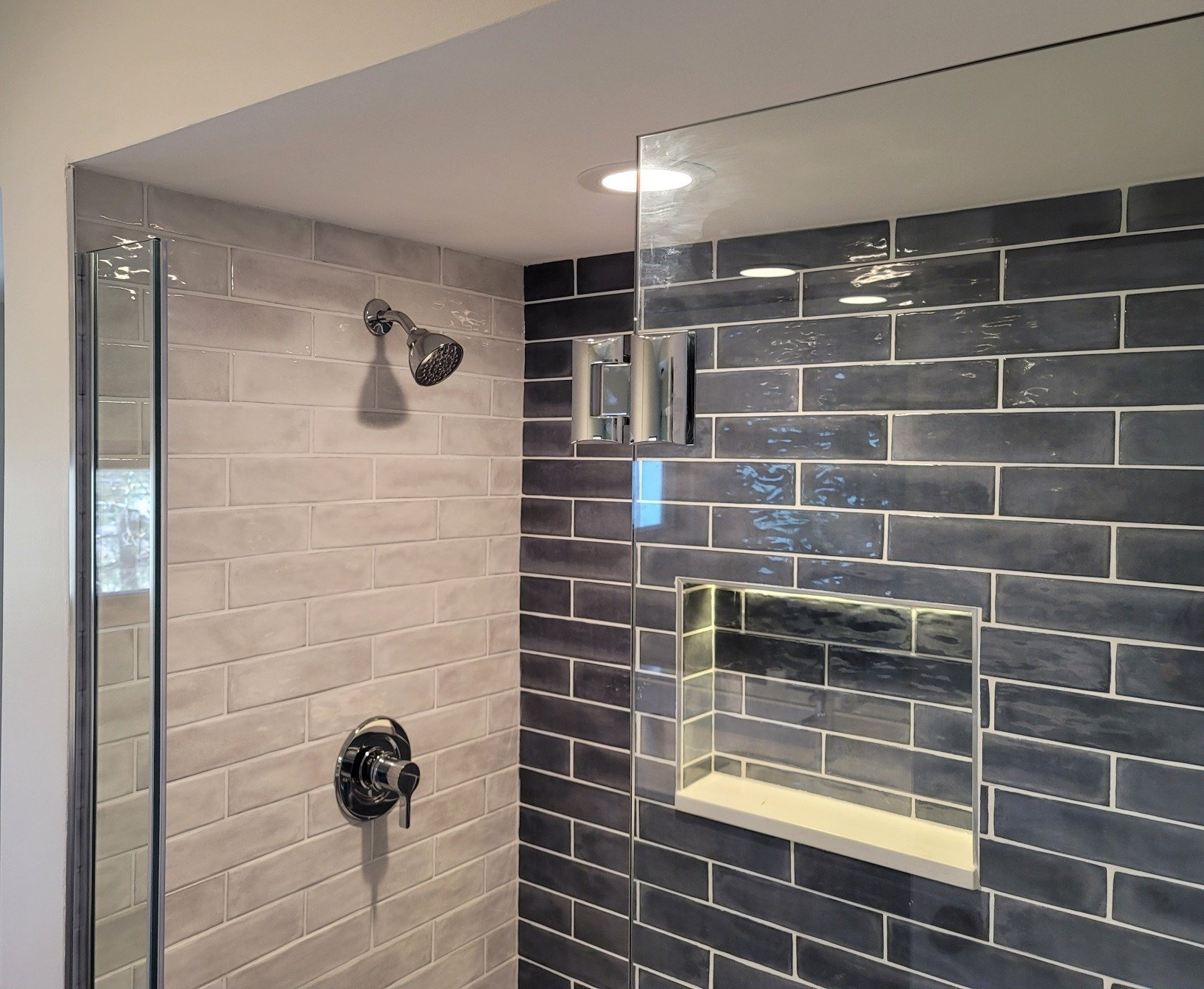 Modern shower with glass door and dark gray brick tile.