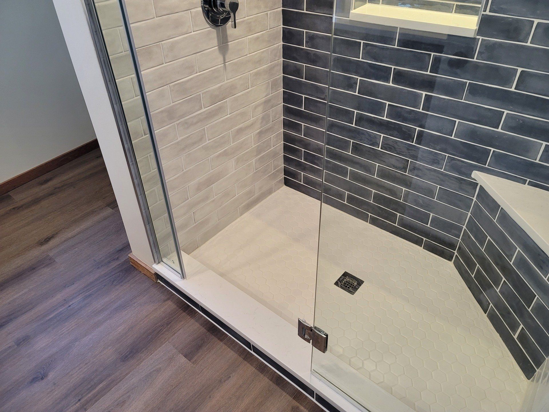 A walk in shower with a glass door and brick walls.