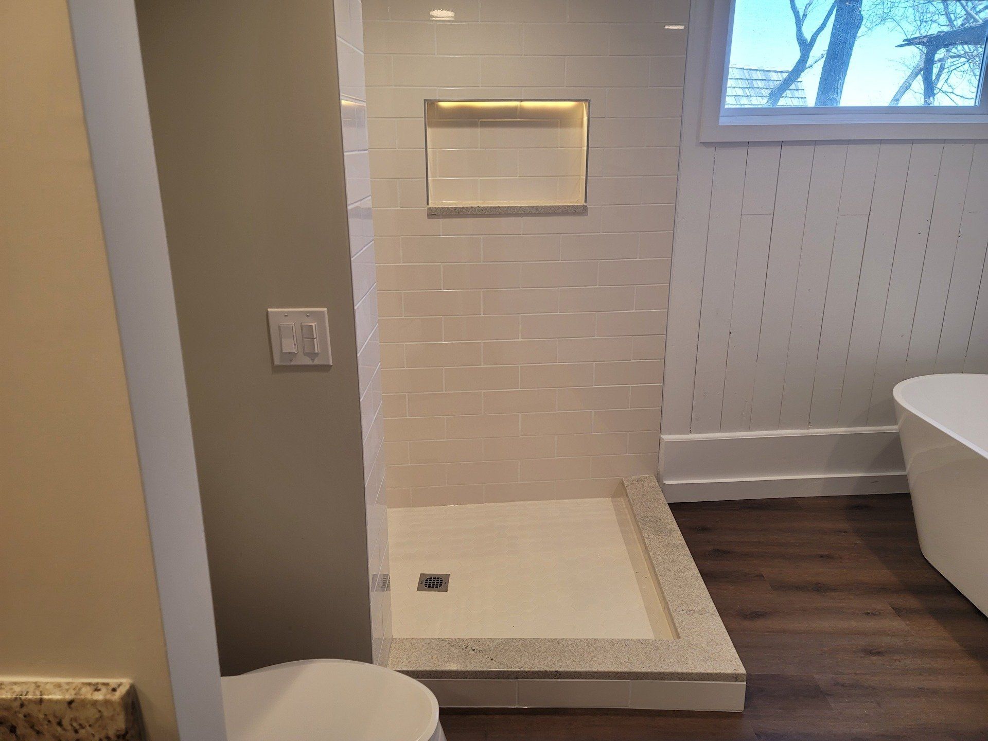 A bathroom with a walk in shower , toilet , tub and window.