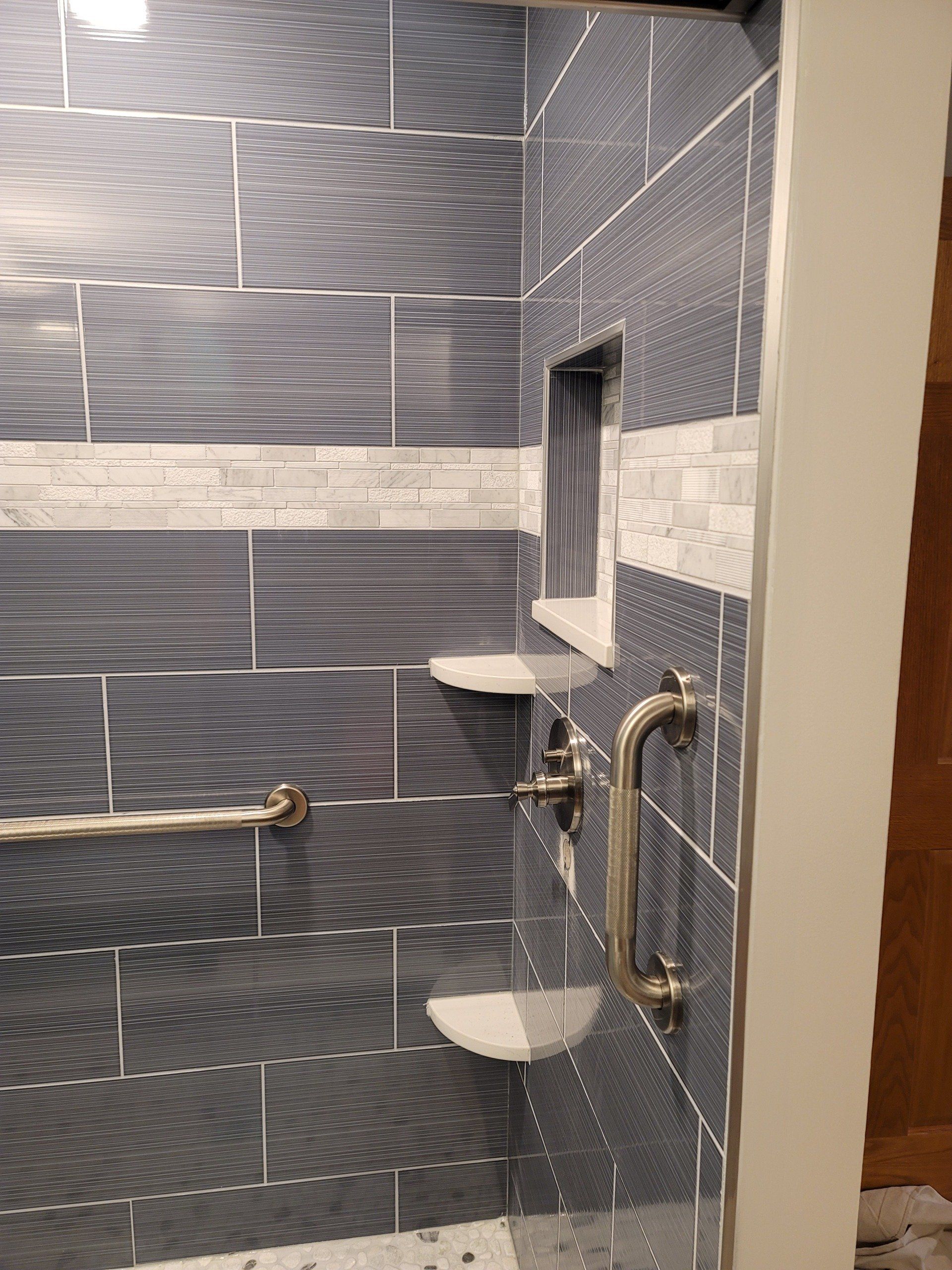 A bathroom with blue tiles and a shower with a hand rail.