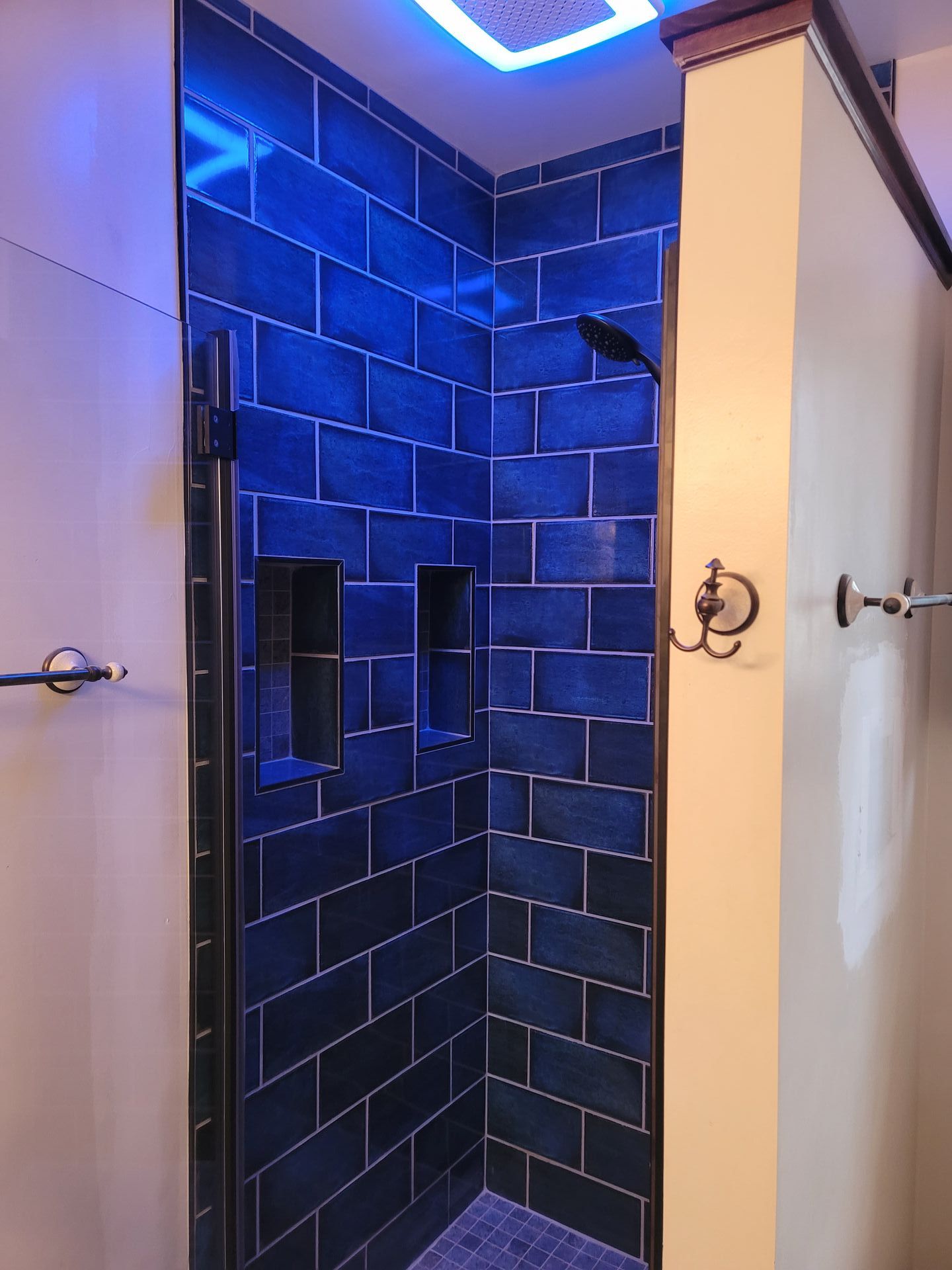 A bathroom with blue tiles and a shower with a blue light on the ceiling.